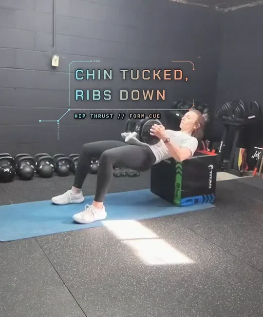 Coach Tabitha doing a dumbbell hip thrust with her upper back on a plyo box, start: hips low