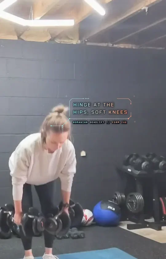 Coach Tabitha holding two dumbbells at the top of a Romanian deadlift, hinge: hips back