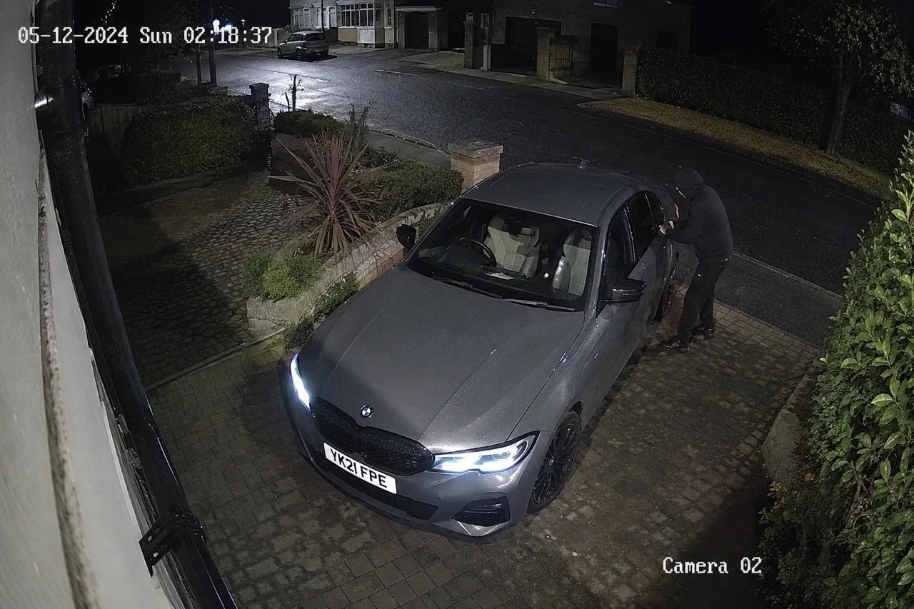 CCTV footage of a hooded thief attempting to break into a grey BMW 3 Series on a UK residential driveway at 02:18 AM