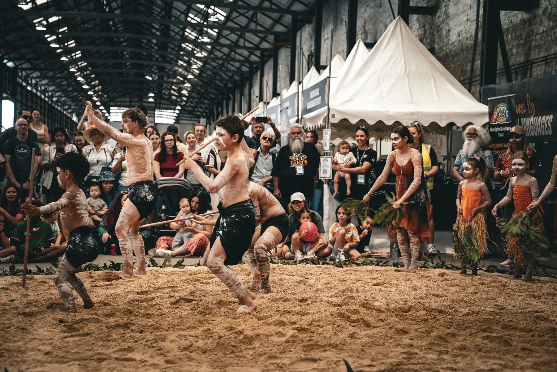 Young dancers performing on a sand floor in front of a crowd