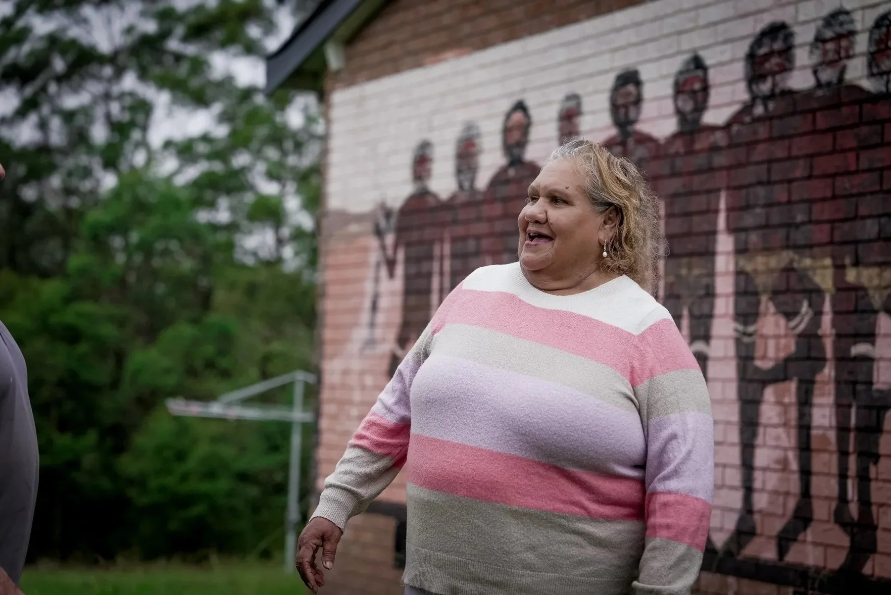 Smiling community member in front of a painted mural