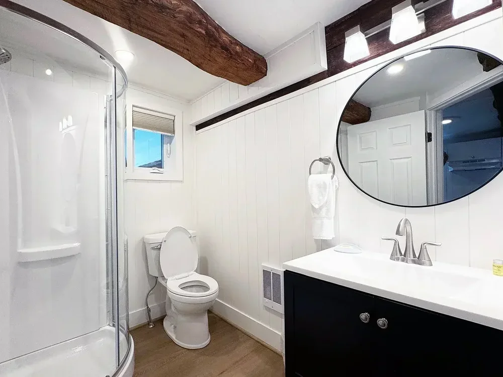 Apartment 19 bathroom with curved glass shower, modern vanity, and exposed beams
