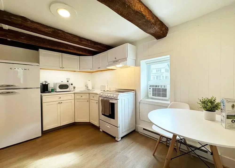 Apartment 19 white kitchen with exposed beams, full-size appliances, and dining table