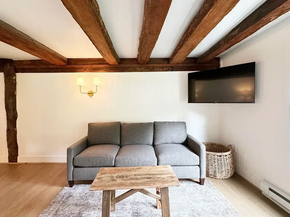 Apartment 19 sitting room with gray sofa, coffee table, Smart TV, and exposed beams