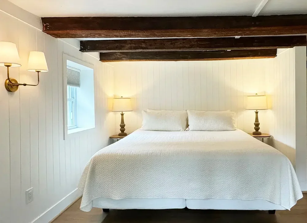Apartment 19 king bedroom with wood-beam ceiling, wall sconces, and white bedding