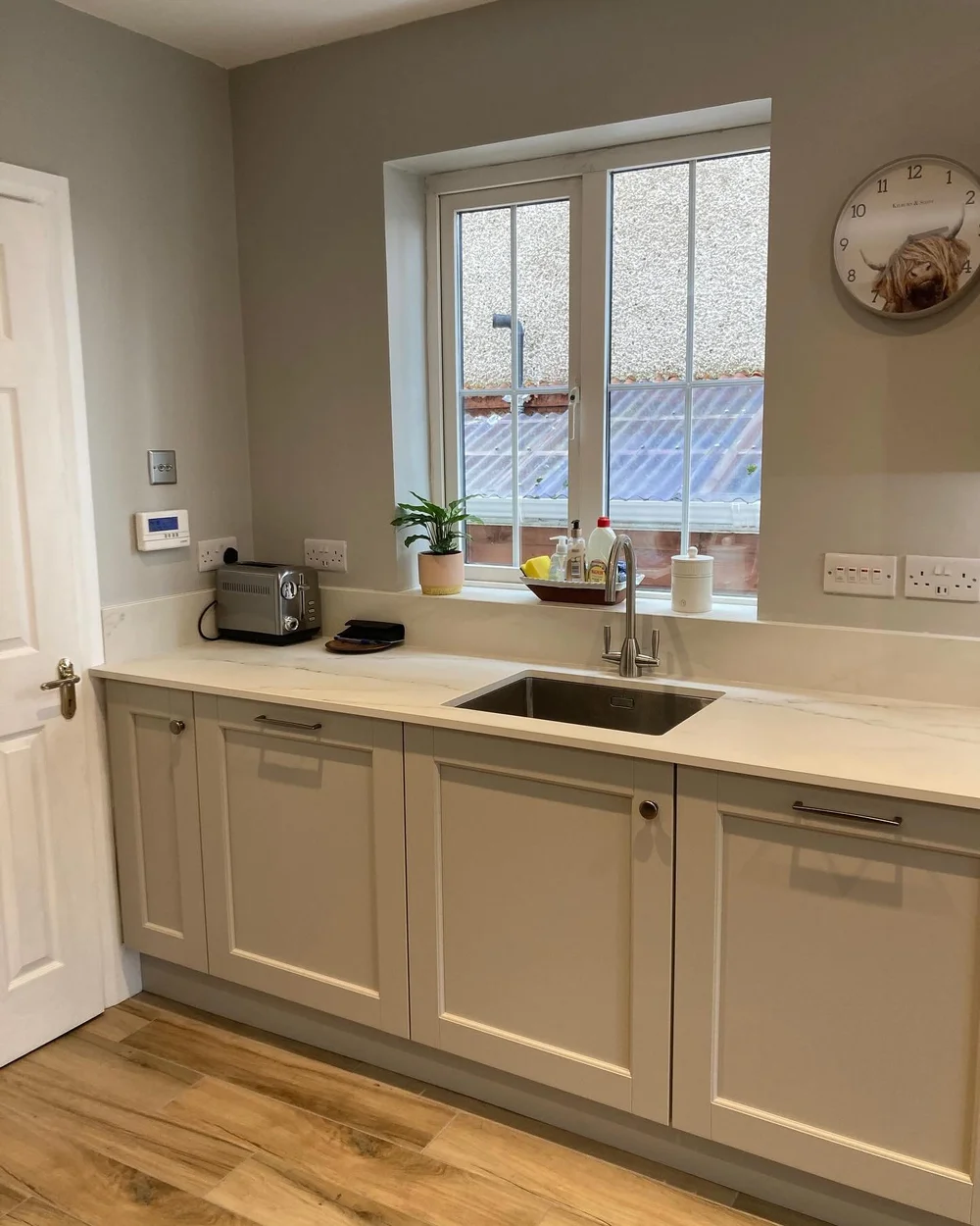 Taupe kitchen cabinetry and a stainless steel sink beneath the window