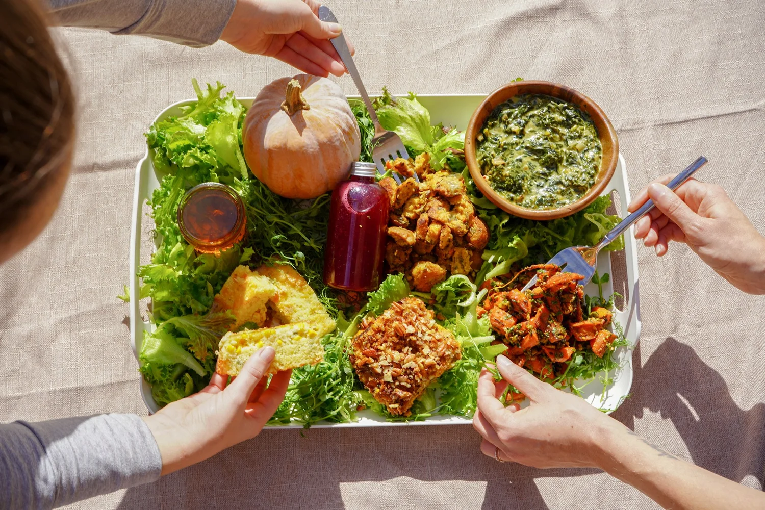 Hands sharing a Thanksgiving platter of greens and roasted vegetables