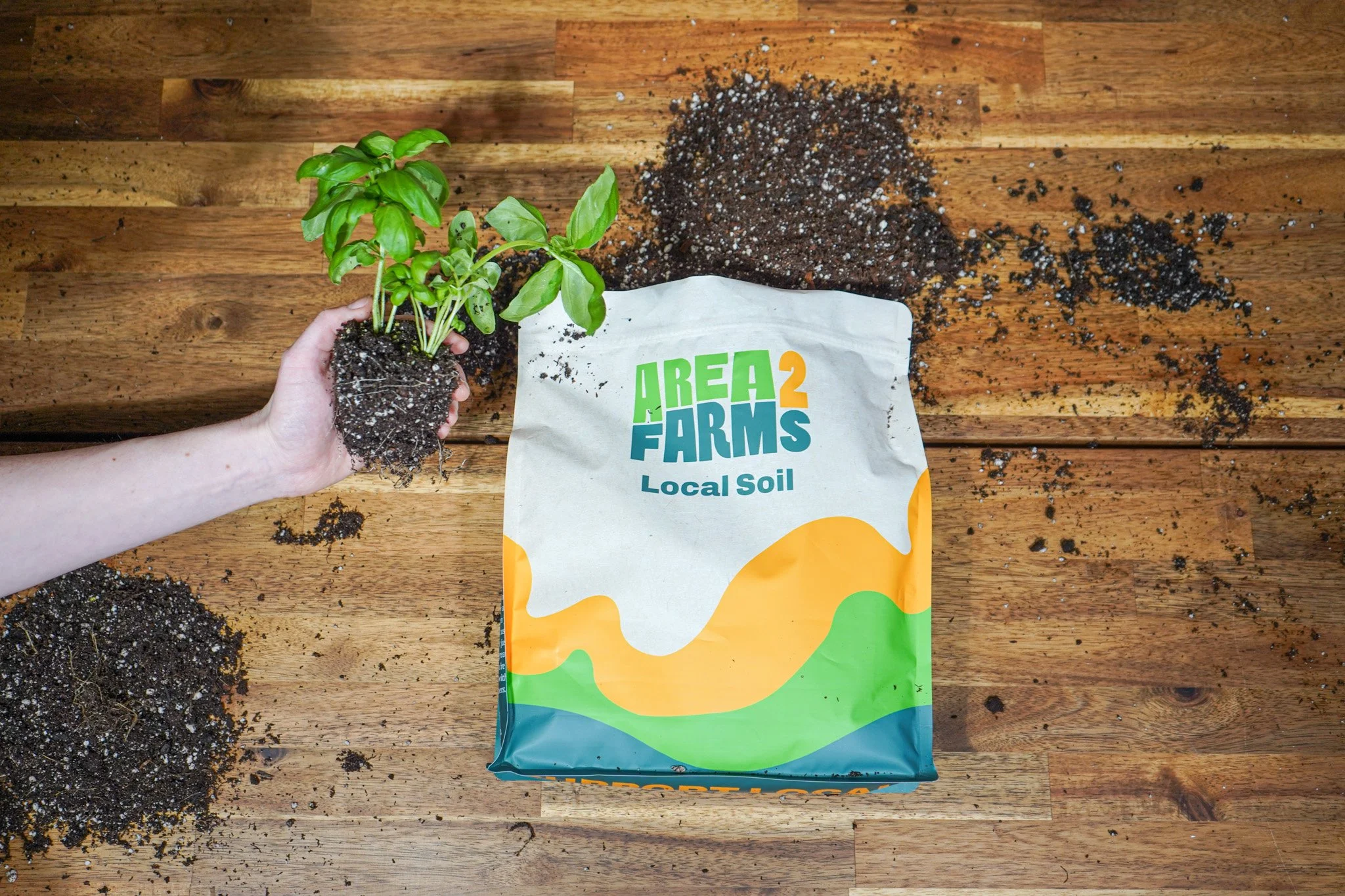 A bag of Area 2 Farms Local Soil beside a basil transplant and fresh composted soil on a workbench