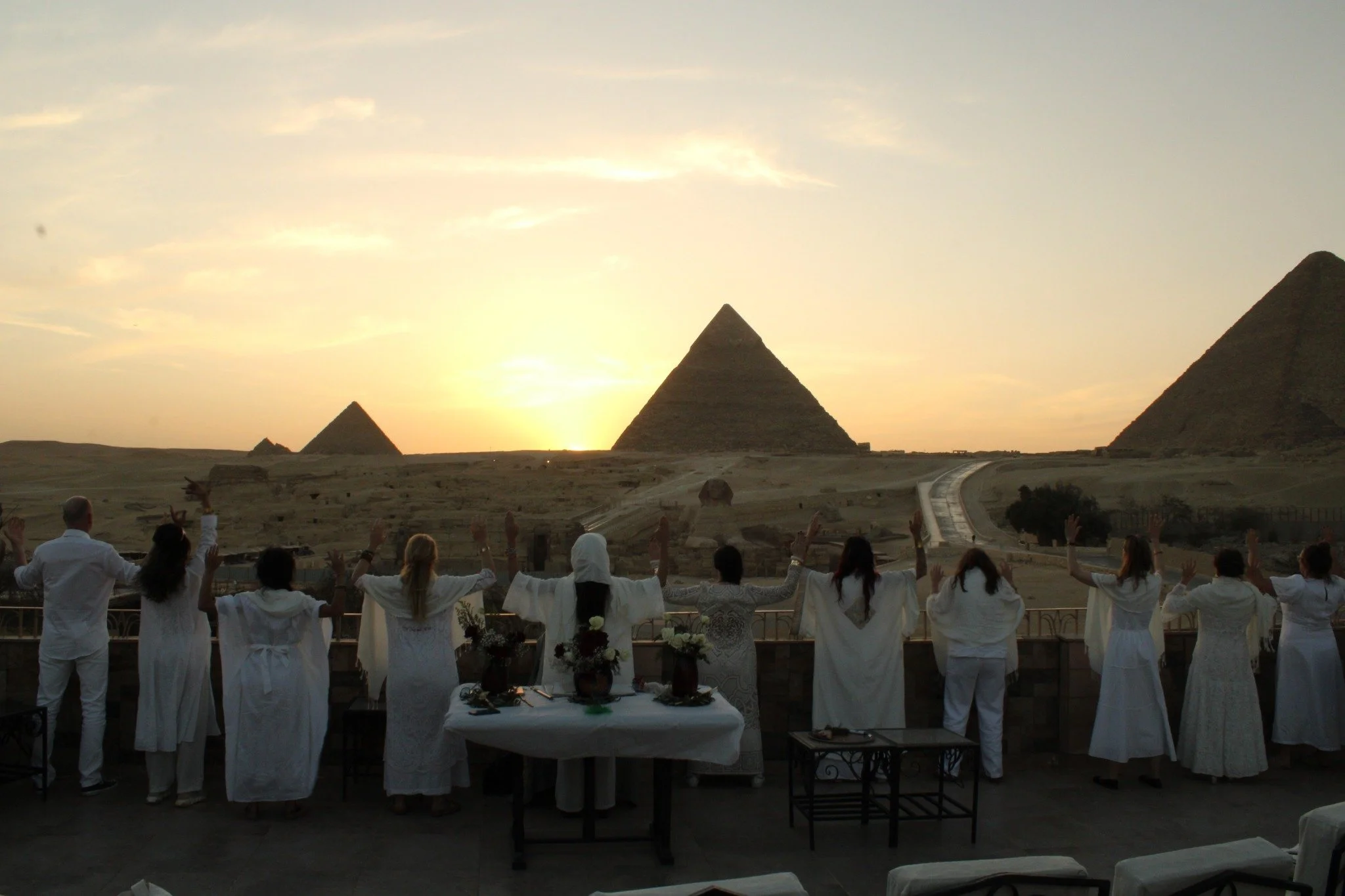 Members of the Order in white standing with raised arms before the pyramids at sunrise