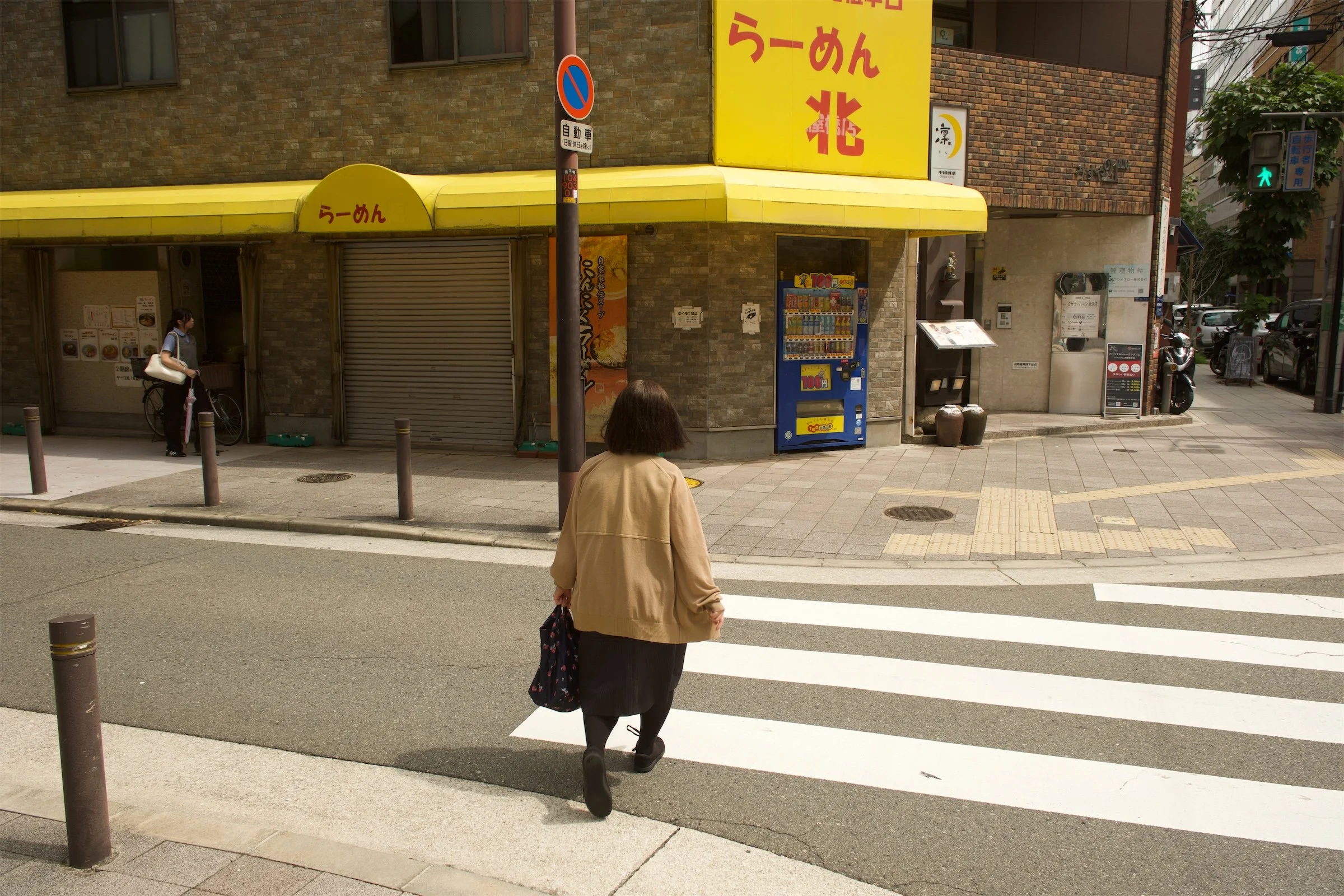 Original street photograph of a yellow storefront and a woman crossing the road