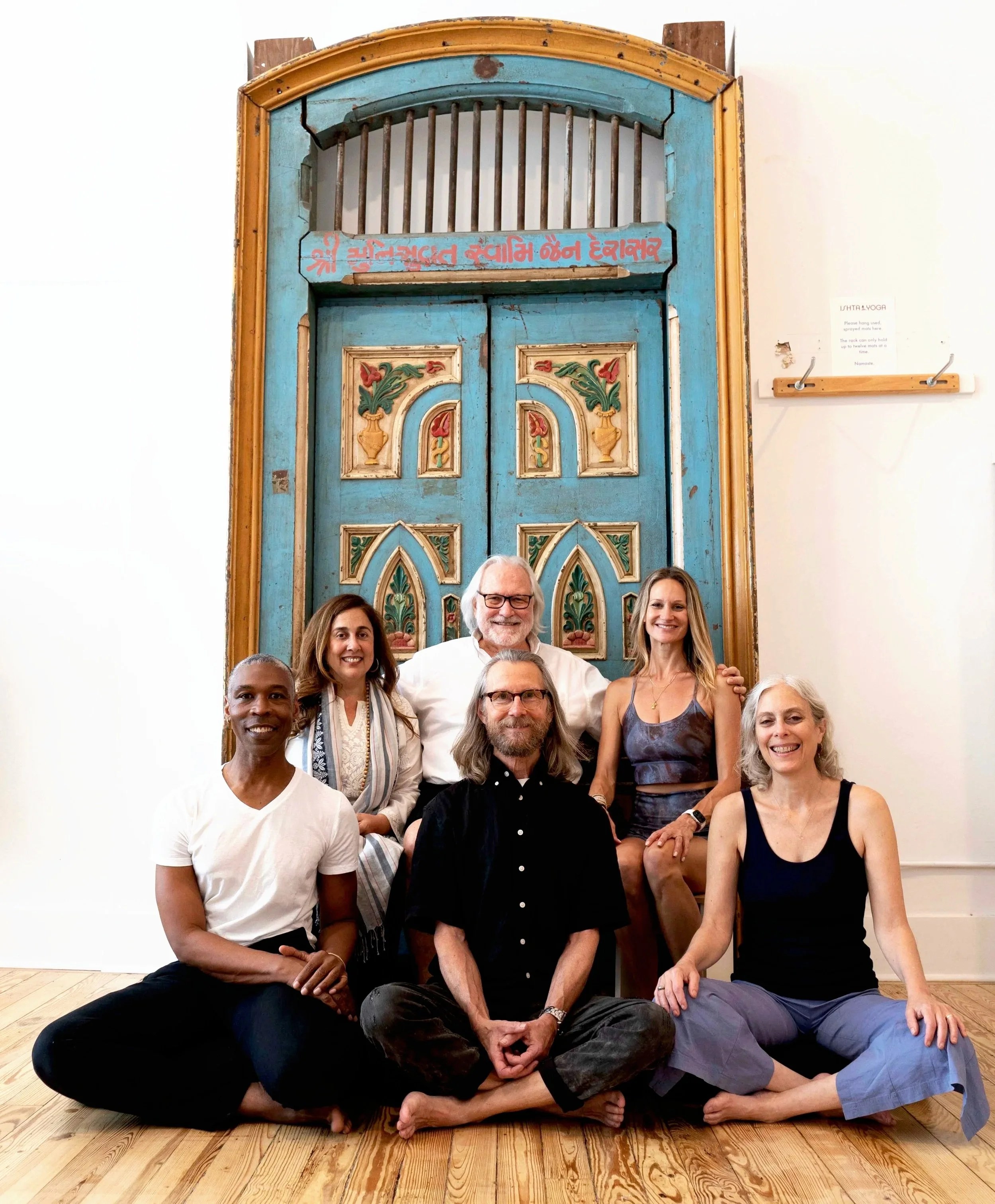 Six ISHTA Yoga teachers seated together in front of the studio’s ornate blue doors in New York City