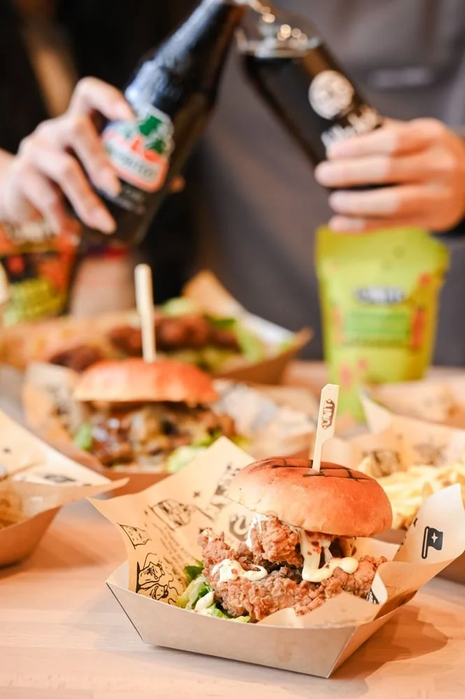 Friends clinking bottles over a Unit chicken burger and fries