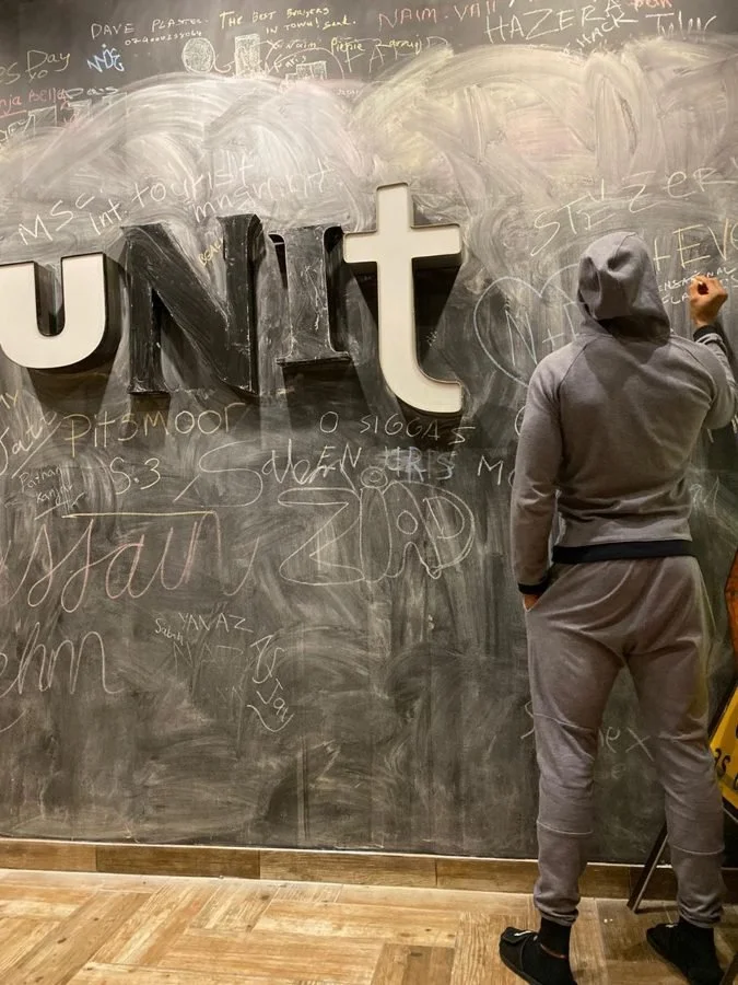 Anthony Joshua writing on the Unit chalk wall beside the big UNIT letters