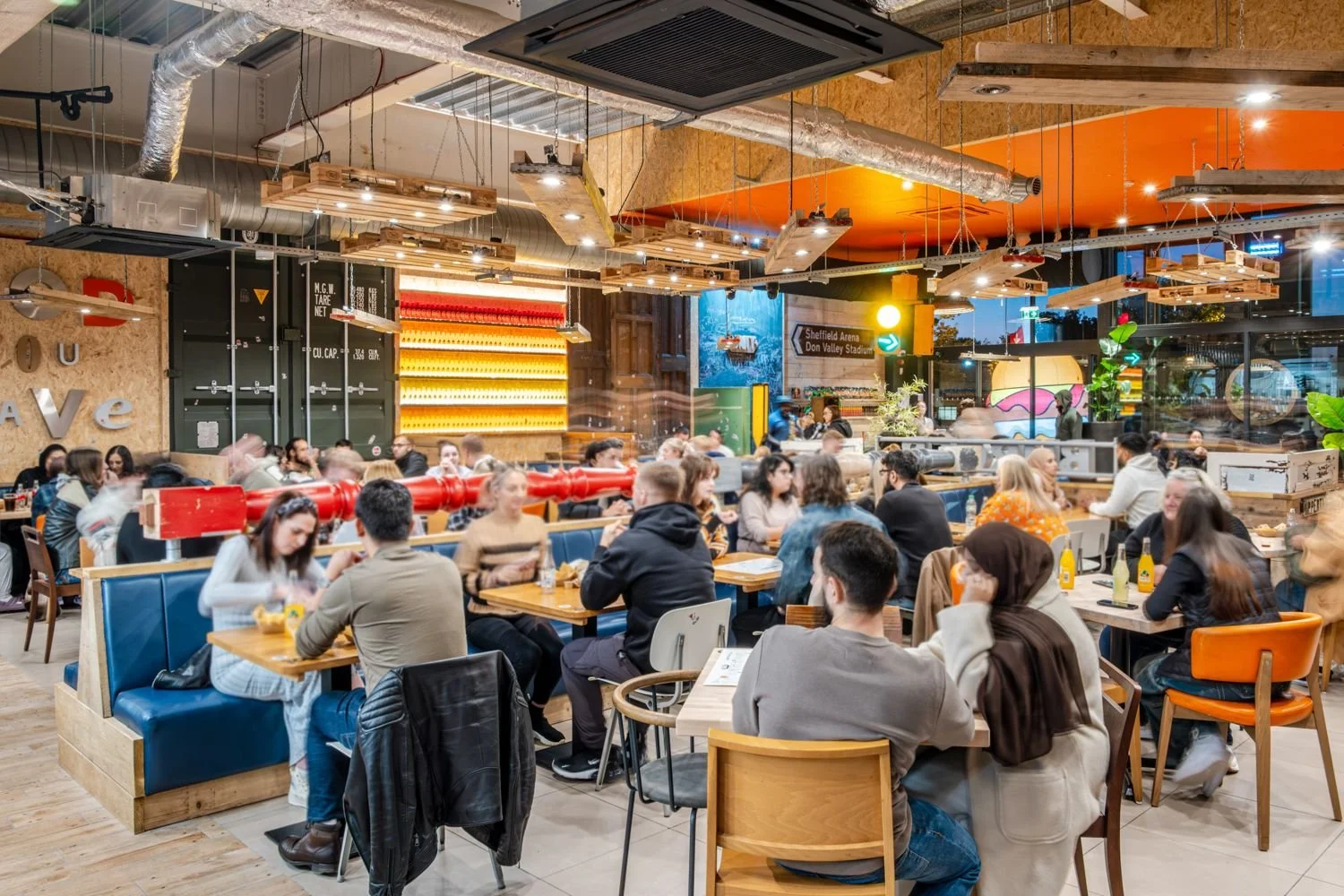 A packed dining room at Unit Valley Centertainment with blue booths, pallet lights and the Food You Crave wall