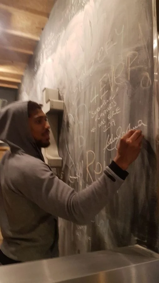 Anthony Joshua signing 'Sensational flavours' on the chalk wall at Unit Headford Street in 2019
