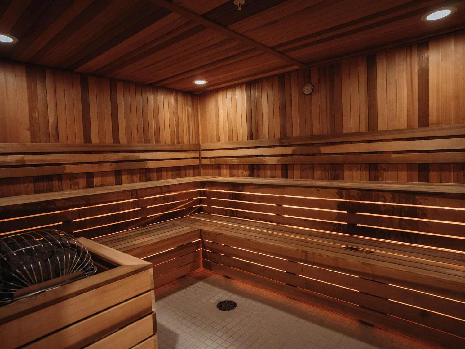 Cedar sauna at Westwood Fitness with tiered benches, backlit seating and a stone heater