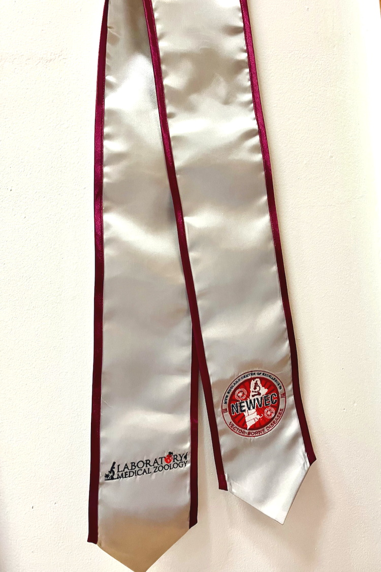 A close up of a graduate in black robes and her stole in UMass colors with the NEWVEC logo on one side, Laboratory of Medical Zoology logo on the other side, and "Class of 2025" below it.