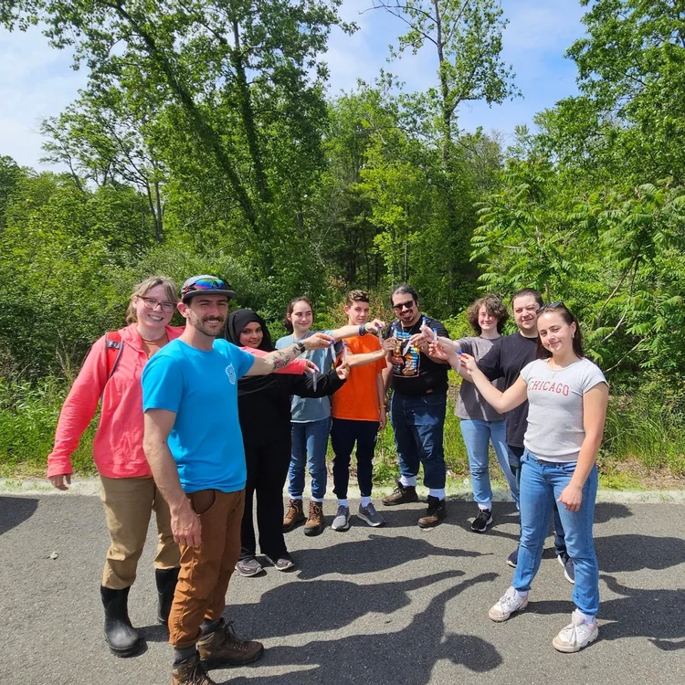 Nine adult students stand in a semi circle holding the tubes of ticks they just collected.