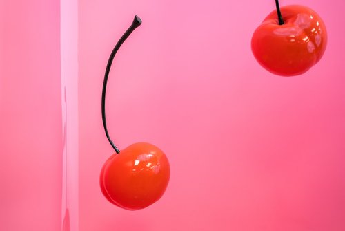 two red cherries with a pink background