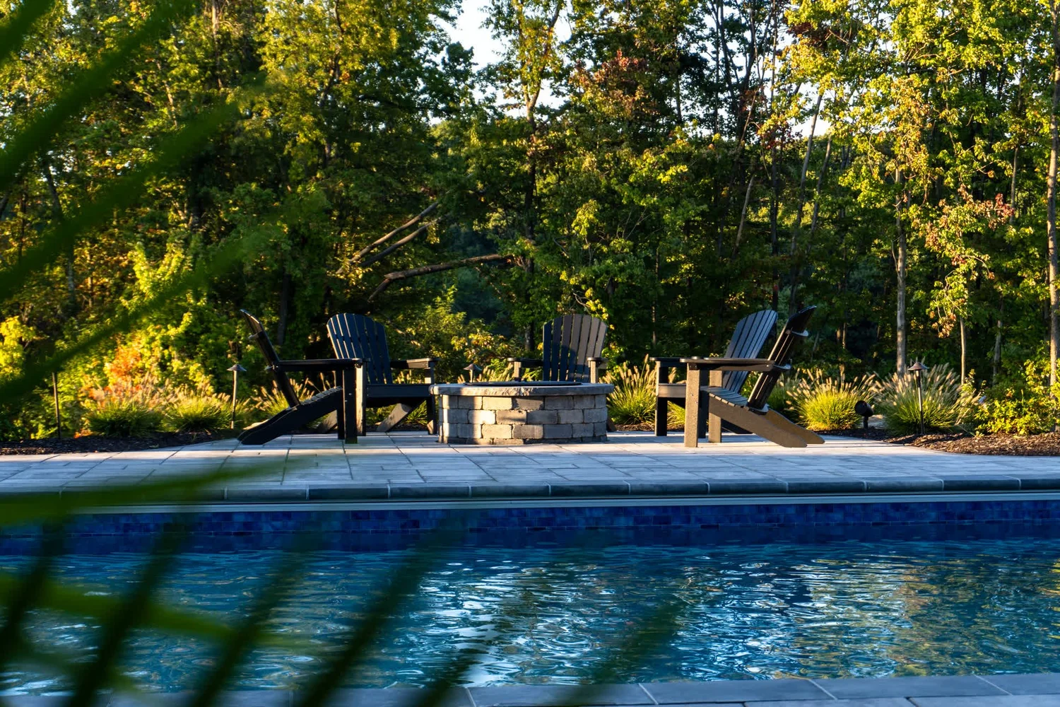 Chairs around a fire pit behind a pool at dusk