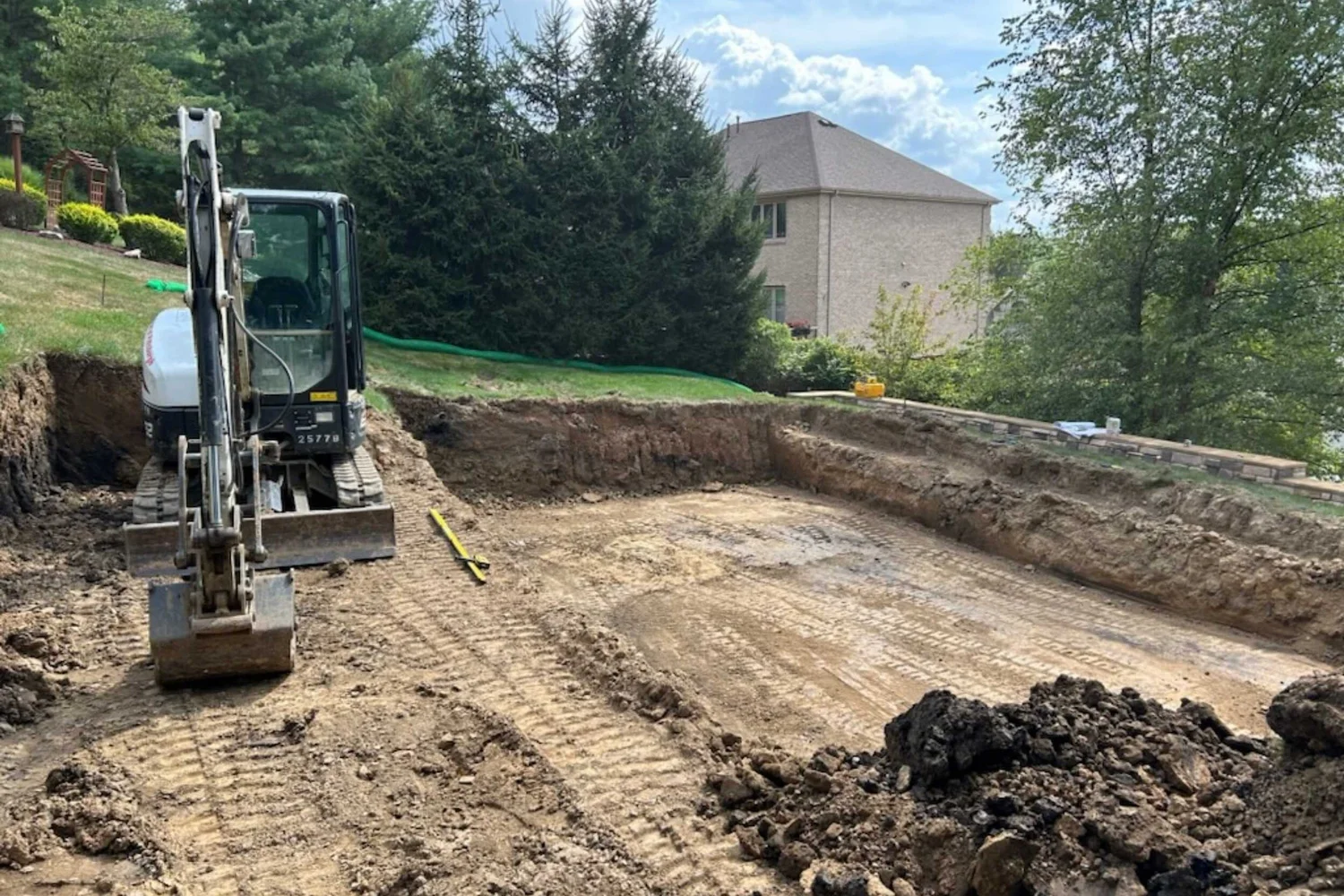 An excavator digging the pool into the lawn at the top of the bank