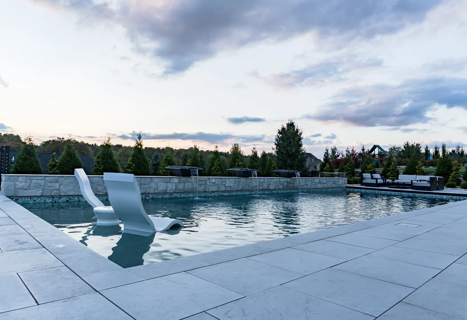 Loungers in the shallow water of a pool, a long stone terrace and an evening sky