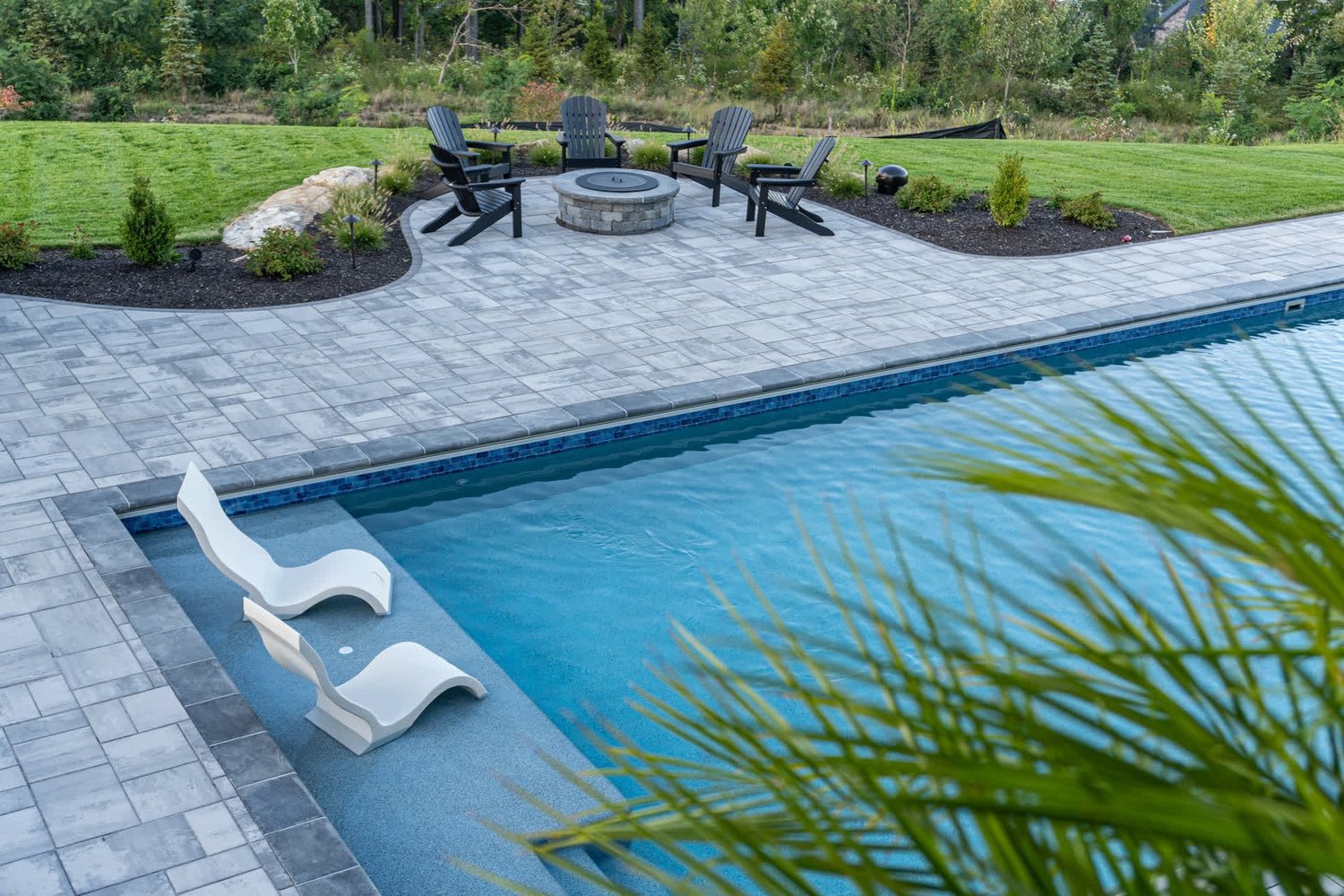 Loungers on the shallow ledge of a pool, a fire pit beyond