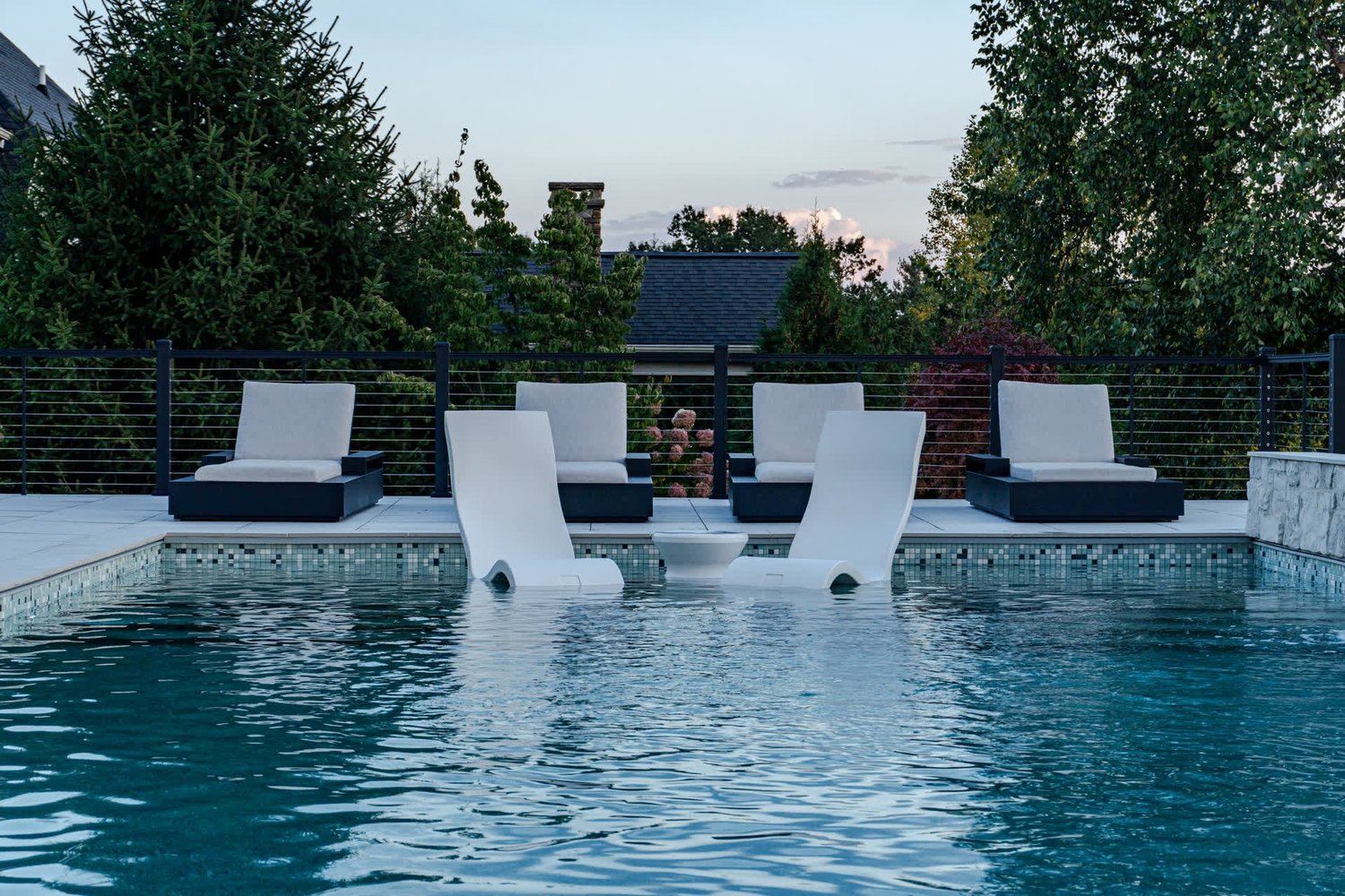 Loungers in the water and on the terrace of a pool at dusk