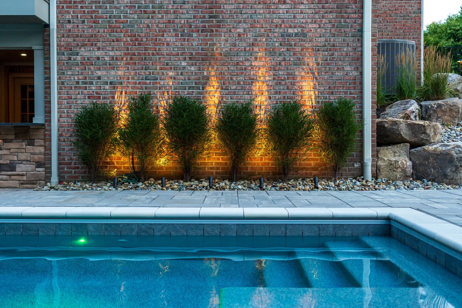Uplit plantings along a brick wall above the pool steps