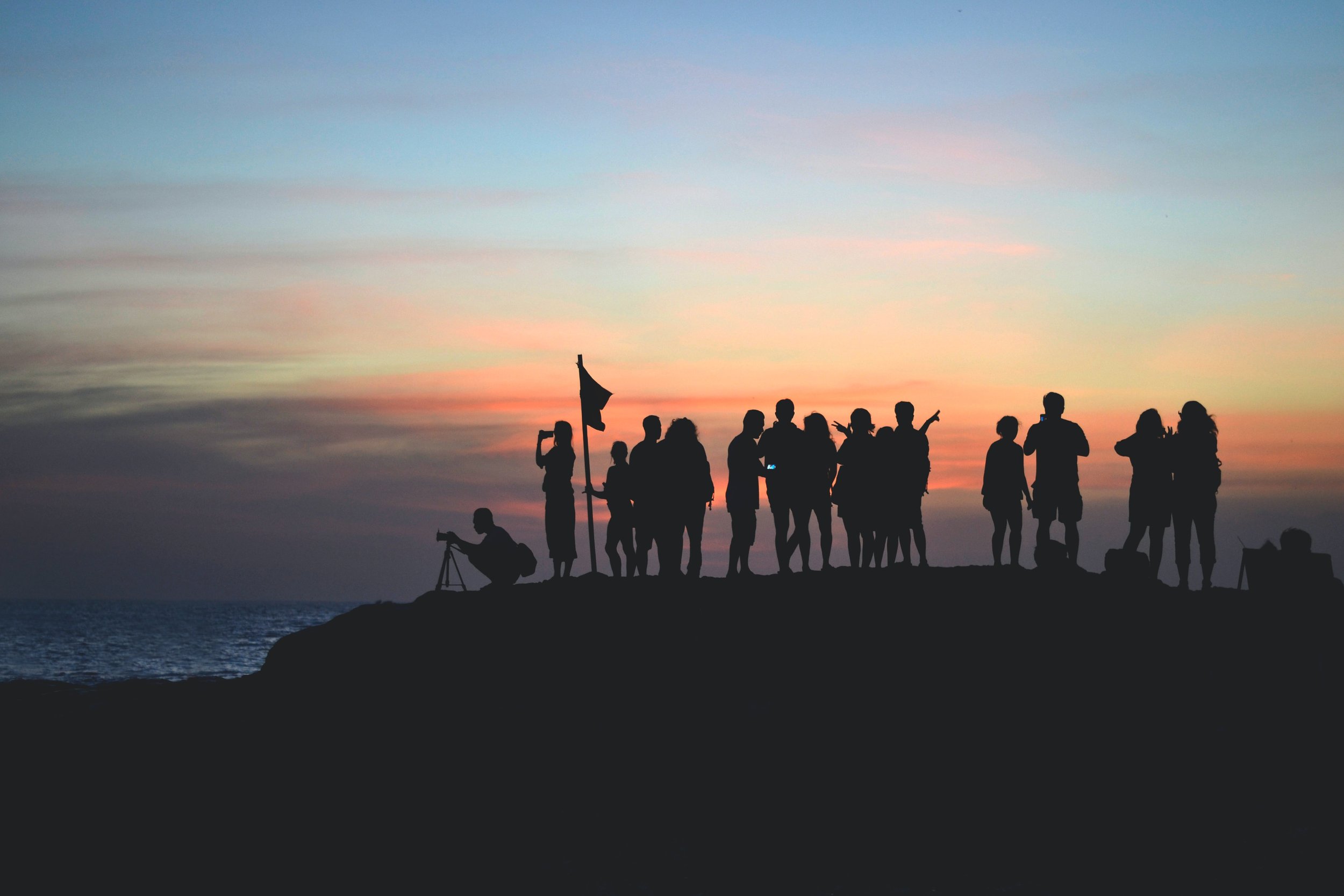 A group of people in silhouette standing on a hilltop overlooking a sunset.