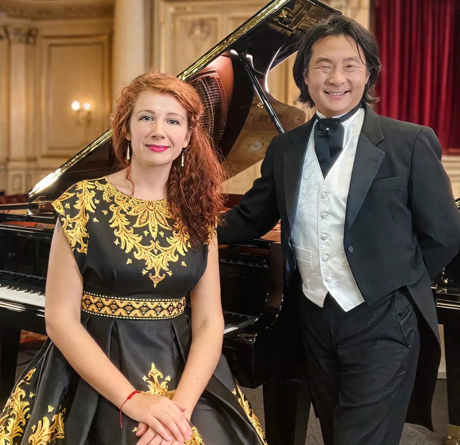 Mada & Hugh Piano Duo in concert dress beside a grand piano