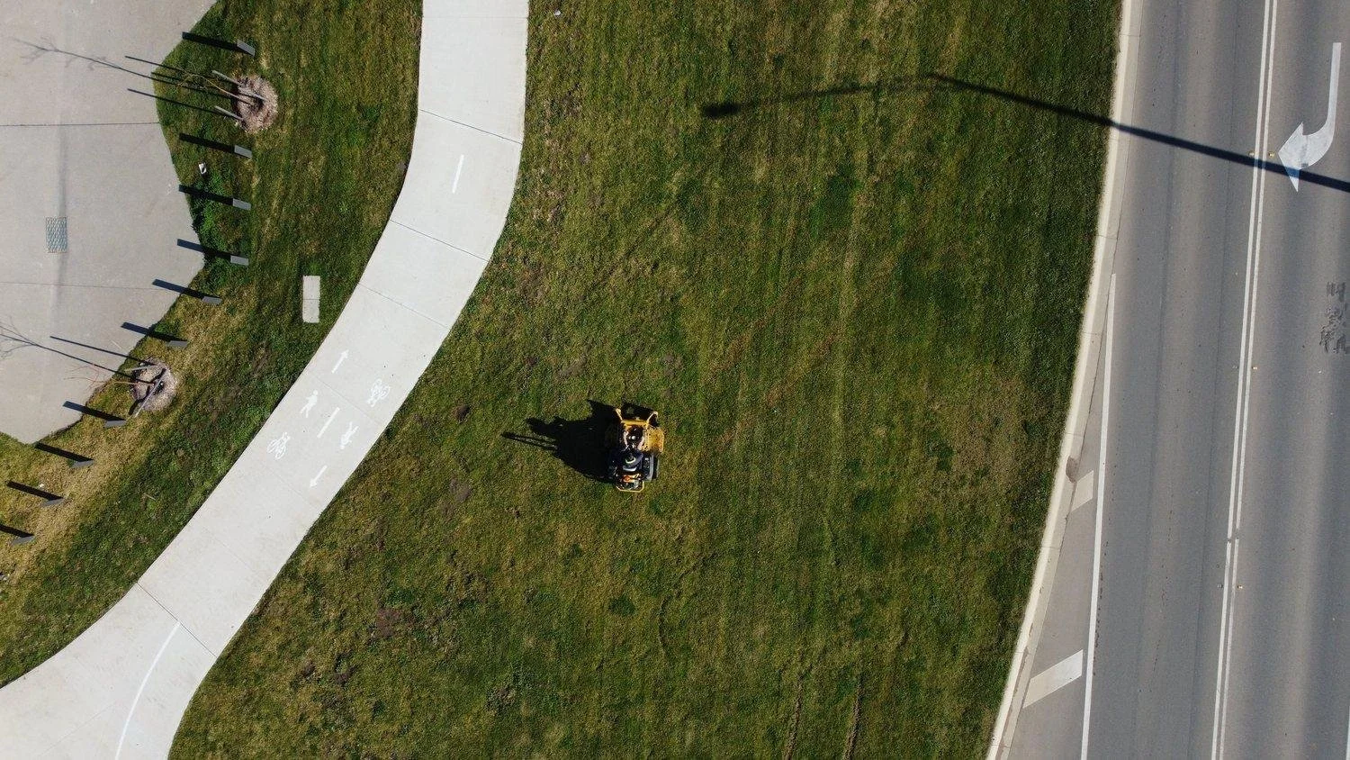 Ride-on mower cutting a large reserve beside a road, from above
