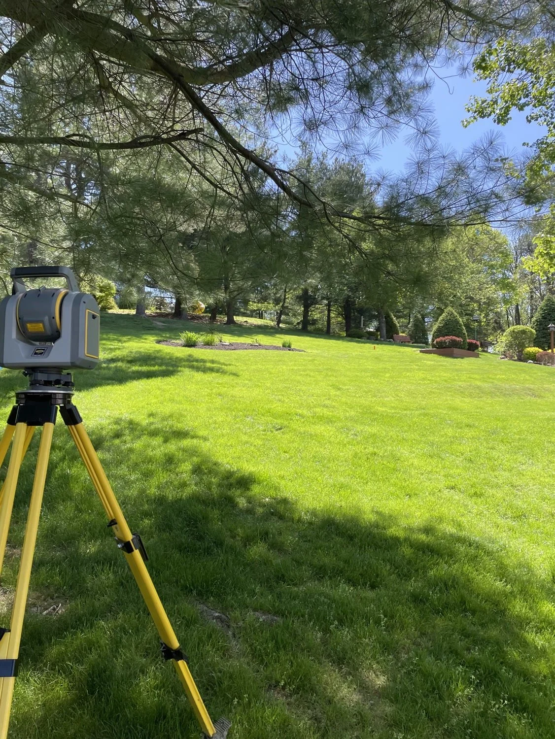 A 3D laser scanner on a yellow tripod on a sloped lawn