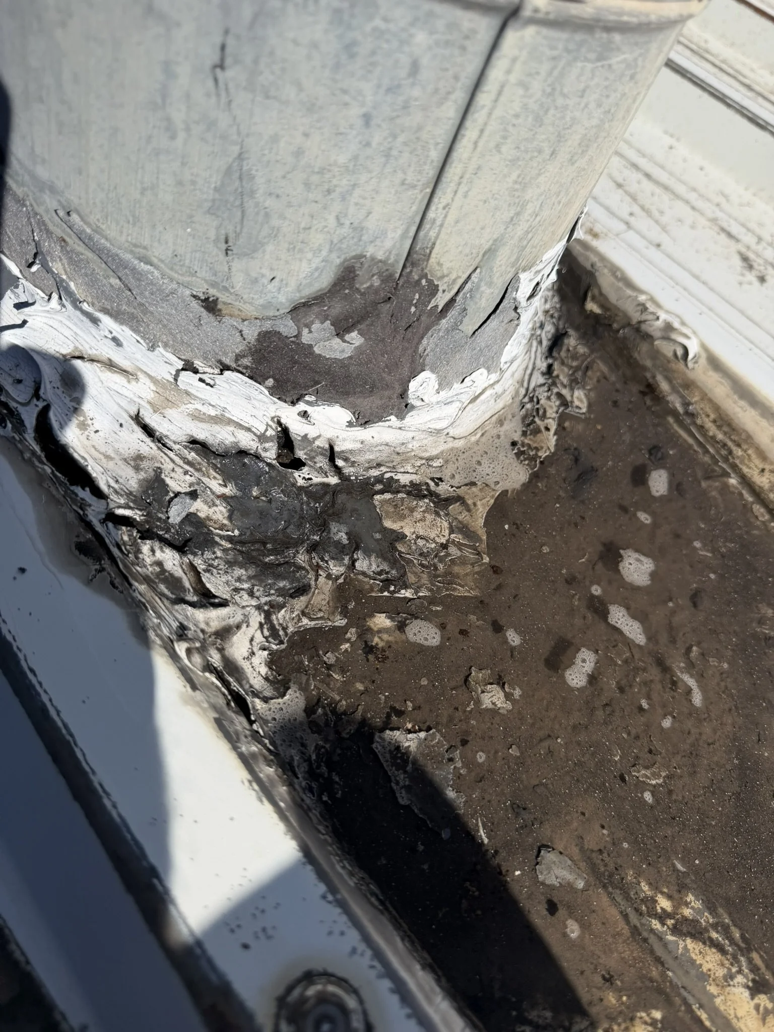 Large galvanized vent pipe with old sealant at its connection to the metal roof.