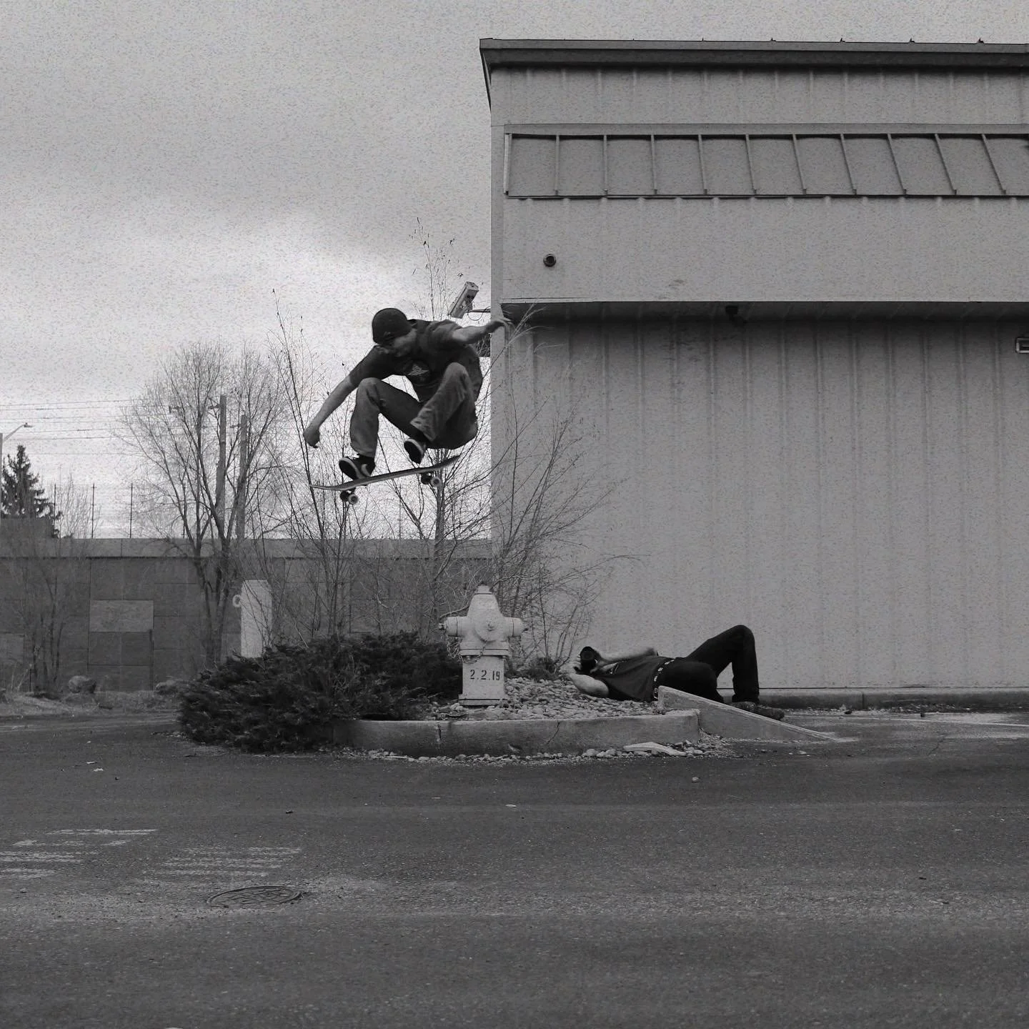 Black and white photograph of Nick doing a kickflip at a DIY skate spot