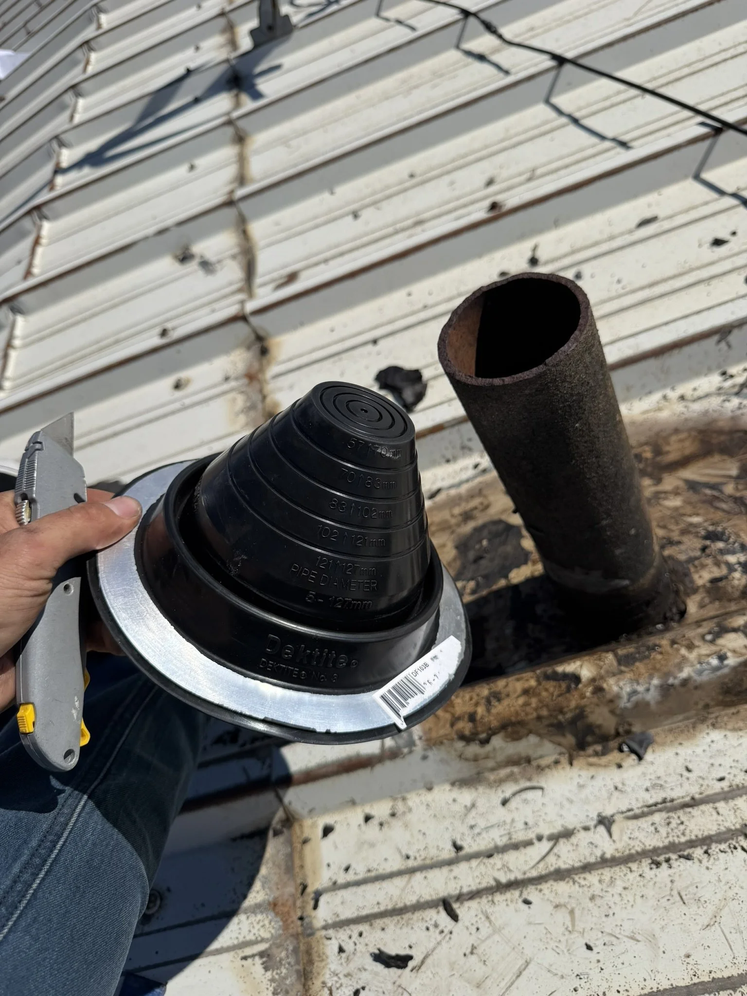 New black flexible pipe boot being sized beside the roof pipe.