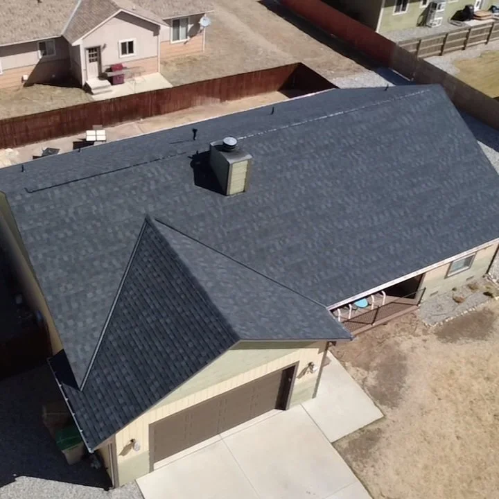 Completed charcoal shingle roof on a tan house, photographed from above