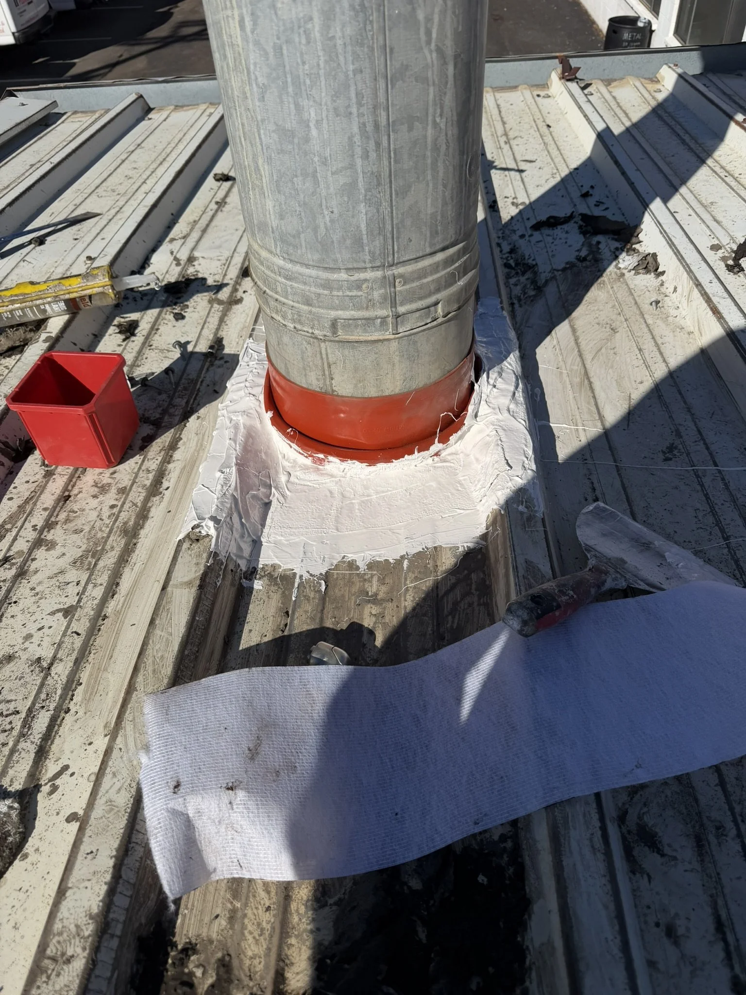 Orange boot around a galvanized vent pipe with white sealant around the flashing base.