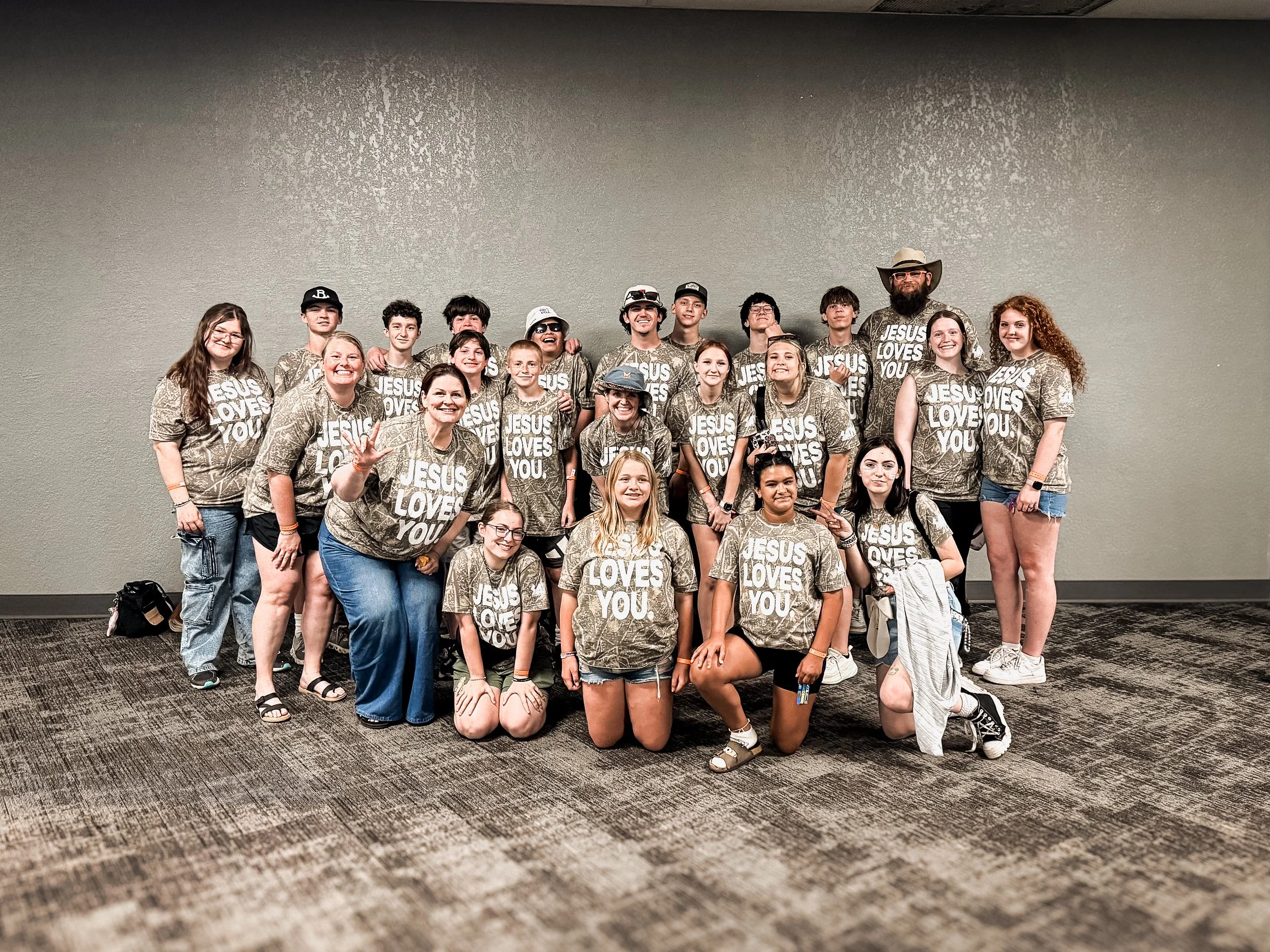 Student ministry group and adult leaders posing together in matching “Jesus Loves You” shirts.