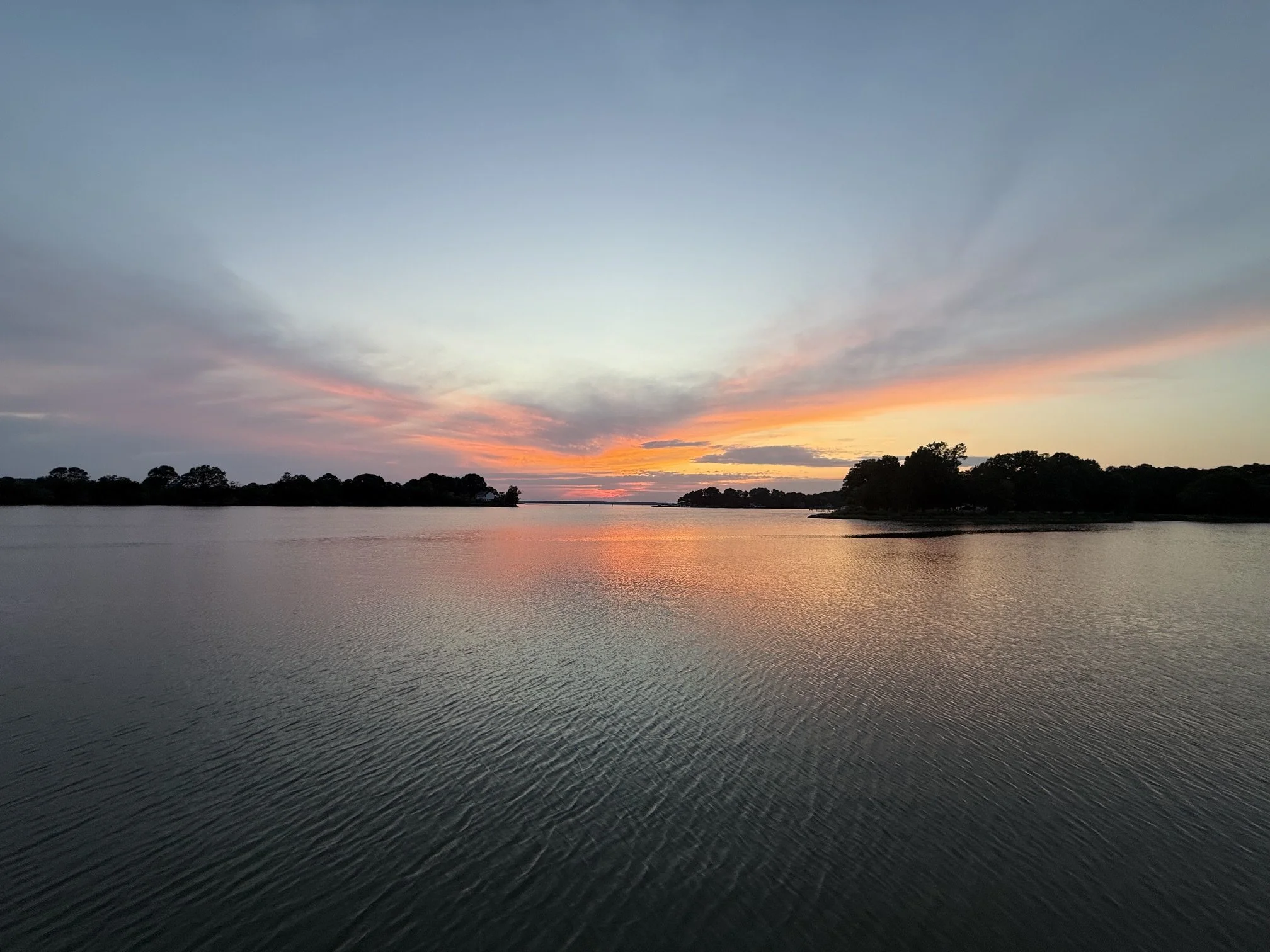 Sunset over calm water and a tree-lined shoreline