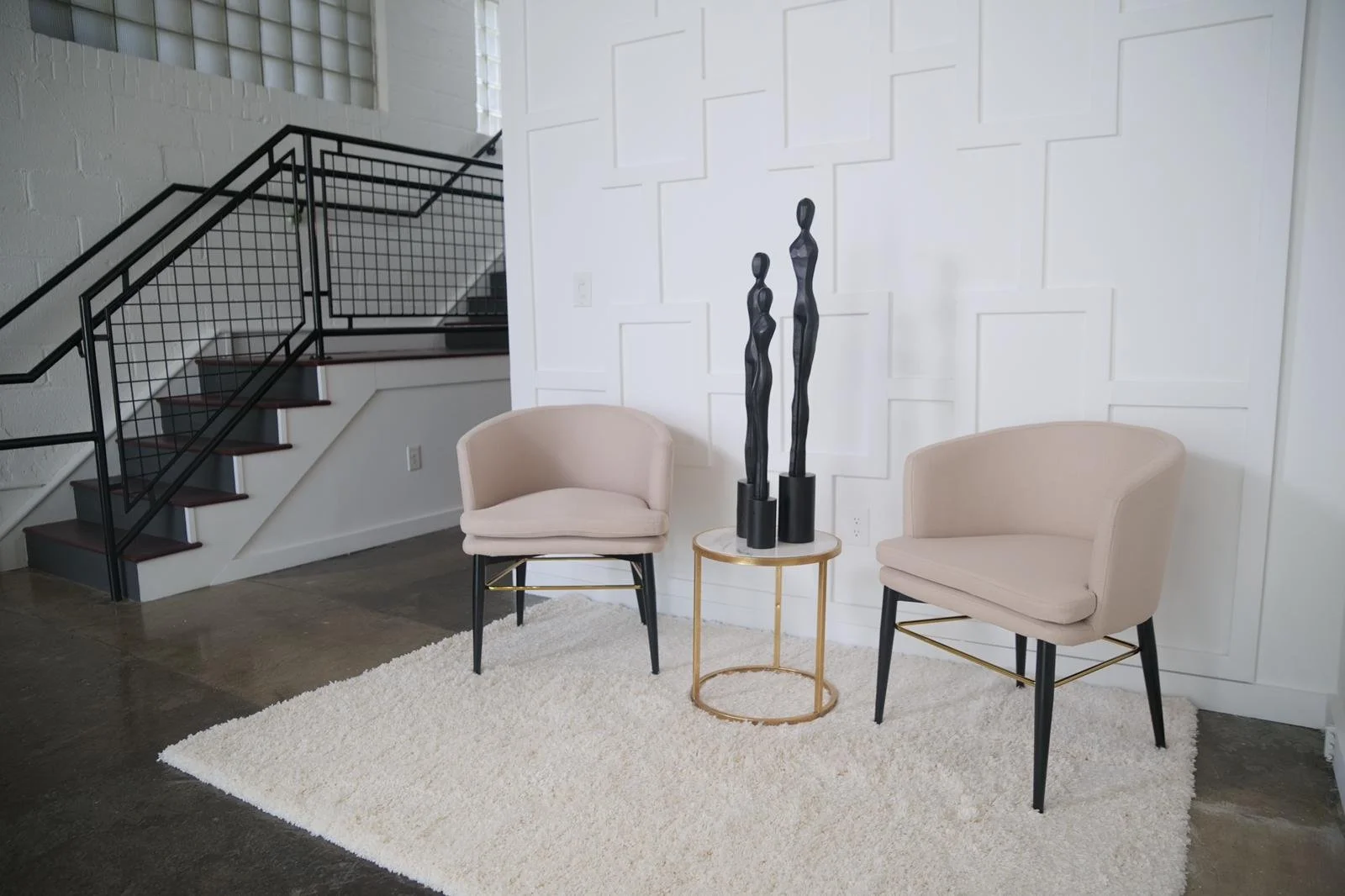 Two cream chairs and a gold side table against the white feature wall.
