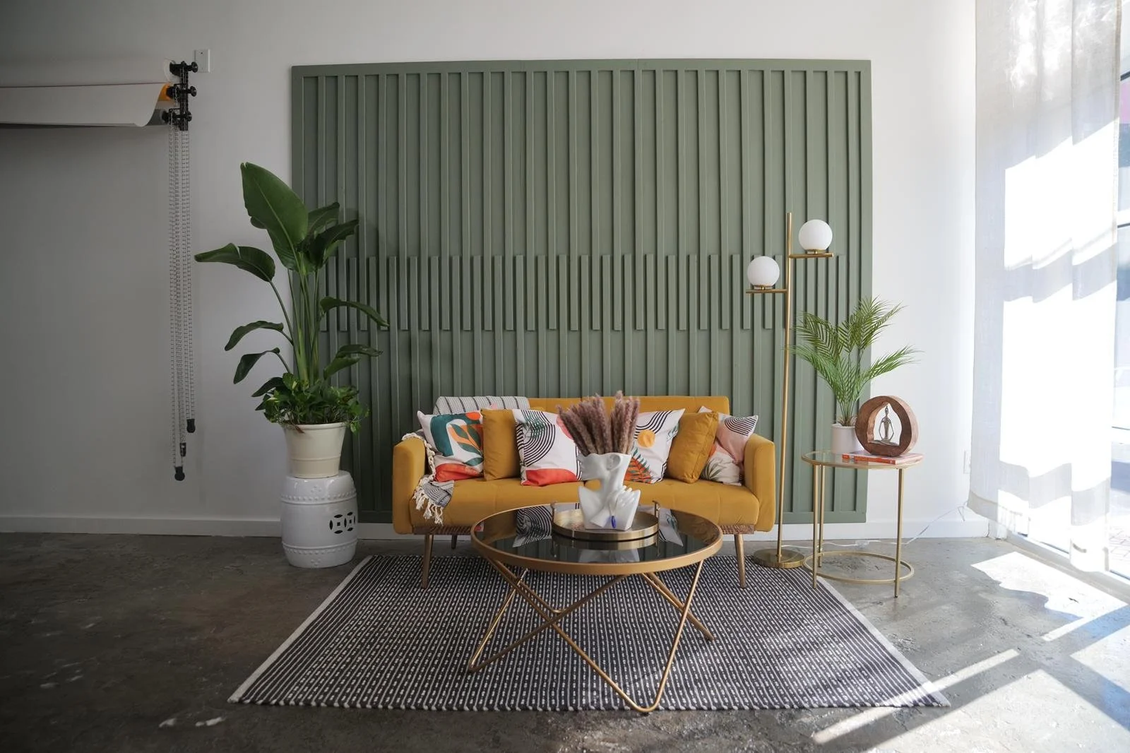 Original yellow sofa, patterned cushions and green feature wall beside tall studio windows.