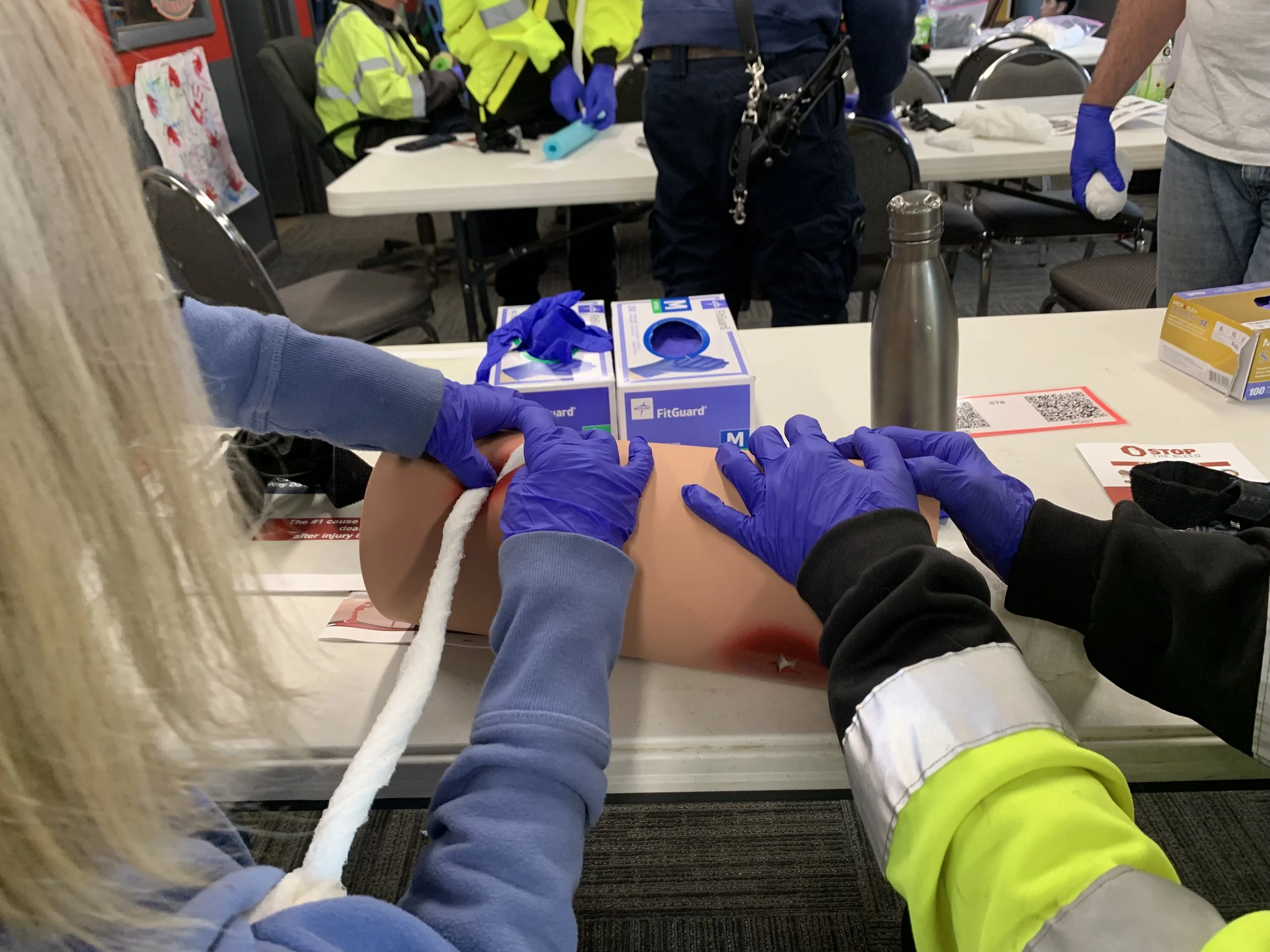 Two people pack wounds with gauze on a foam limb inside the fire station