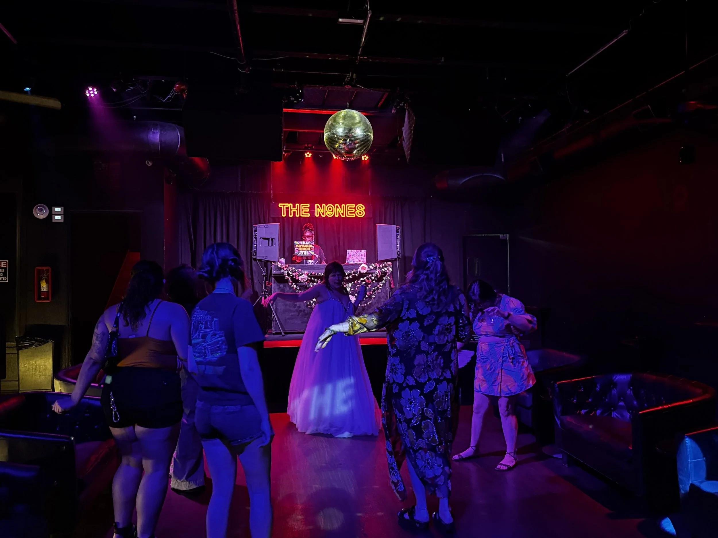People dancing beneath colorful lights and a disco ball at The Nines in Deep Ellum.