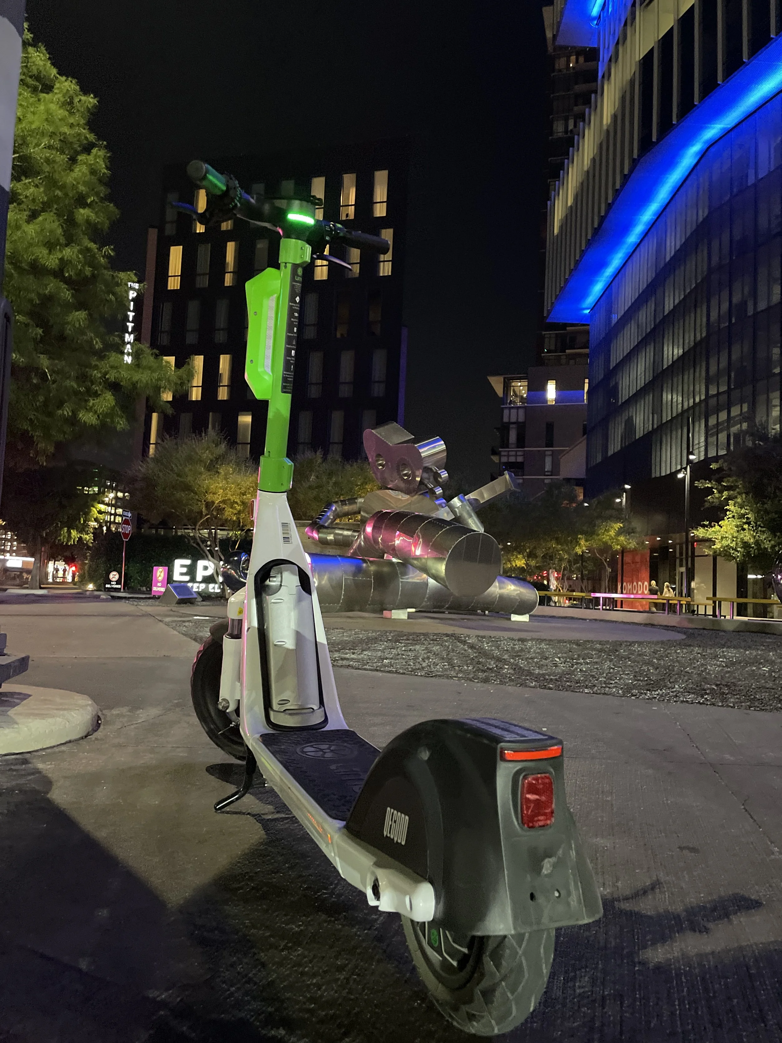 A parked green scooter near public art and illuminated buildings in Deep Ellum.