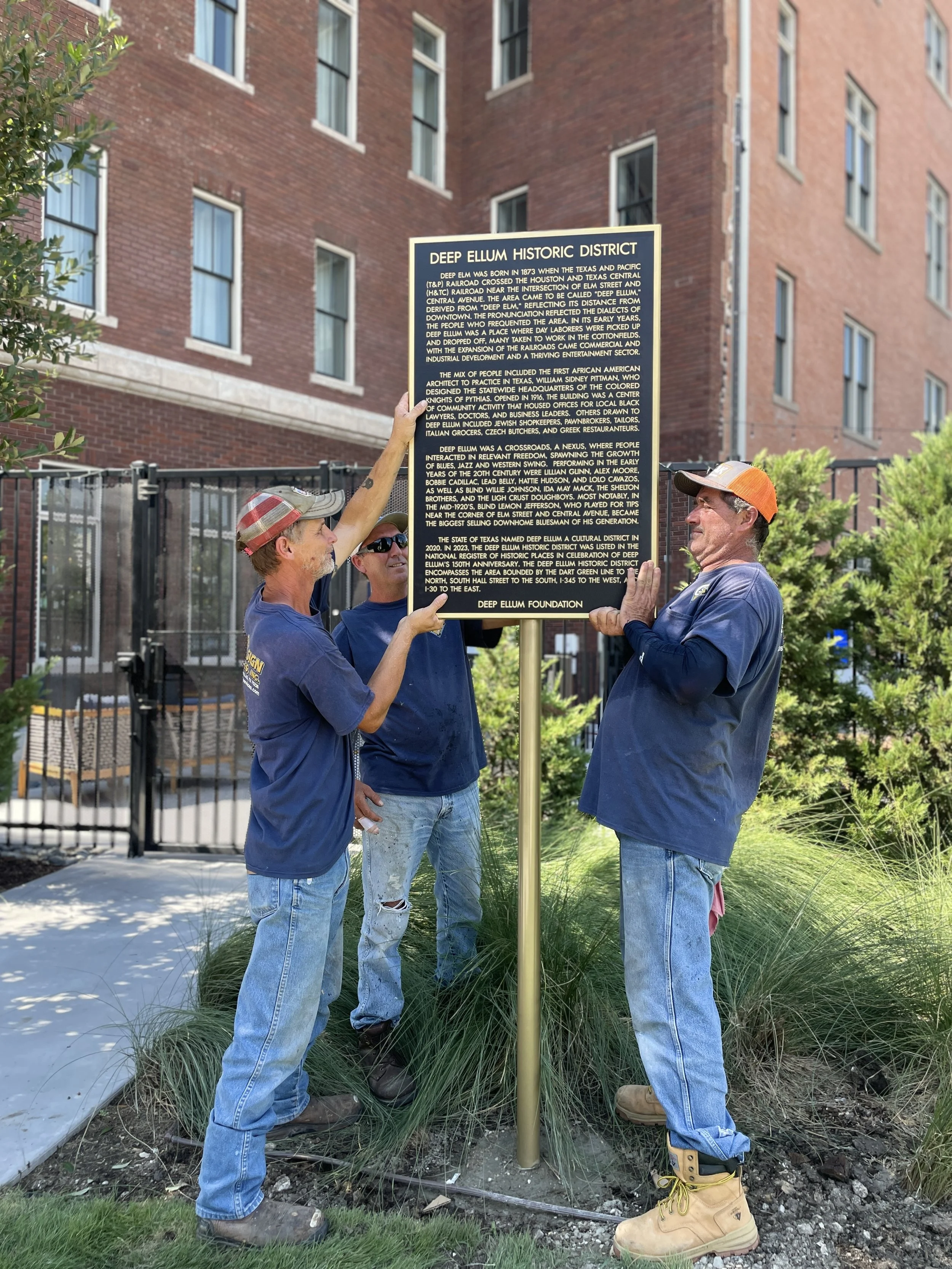 Three people installing a Deep Ellum Historic District marker.