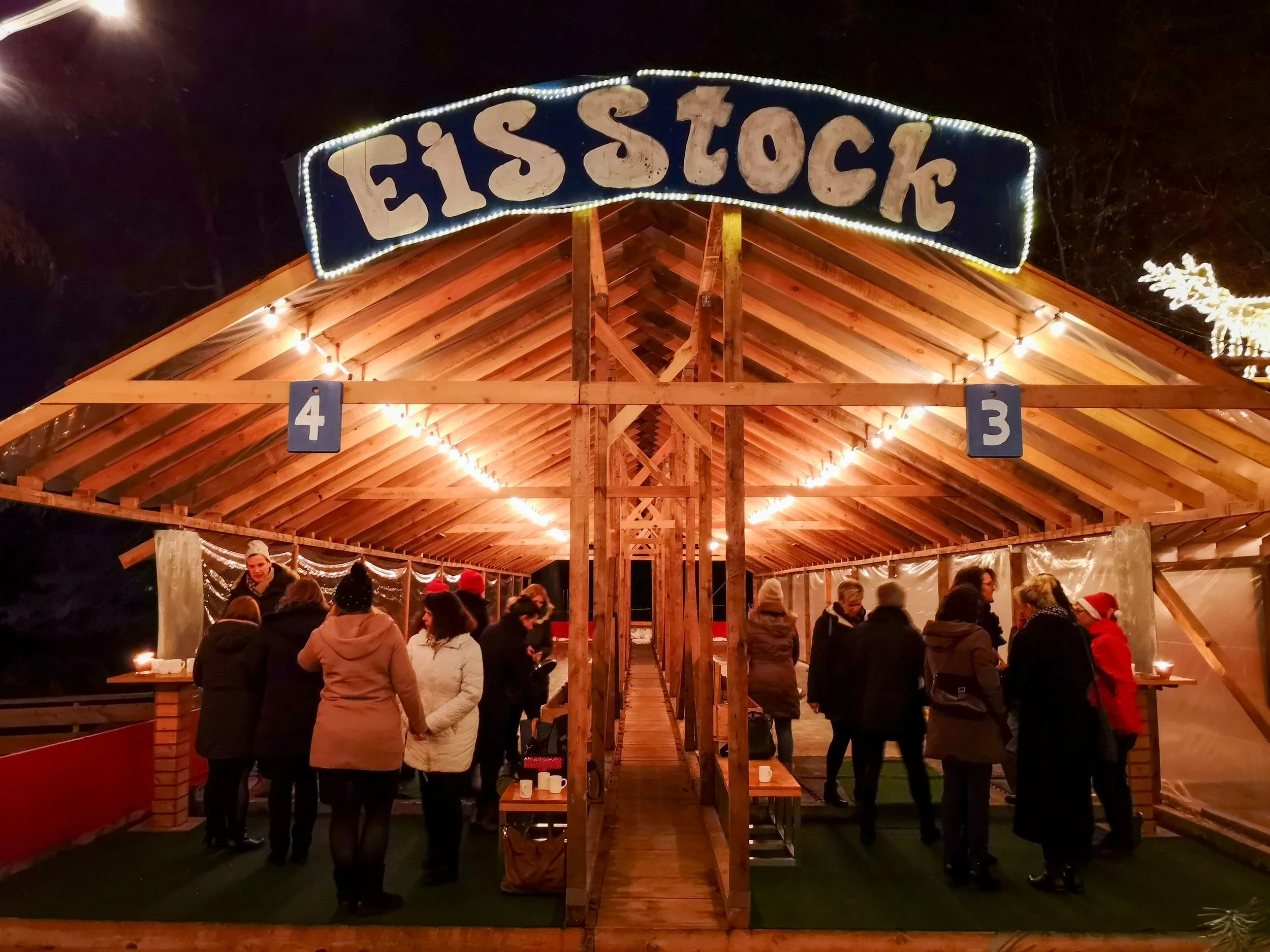 Beleuchtete Eisstock-Hütte mit Gästen am Abend