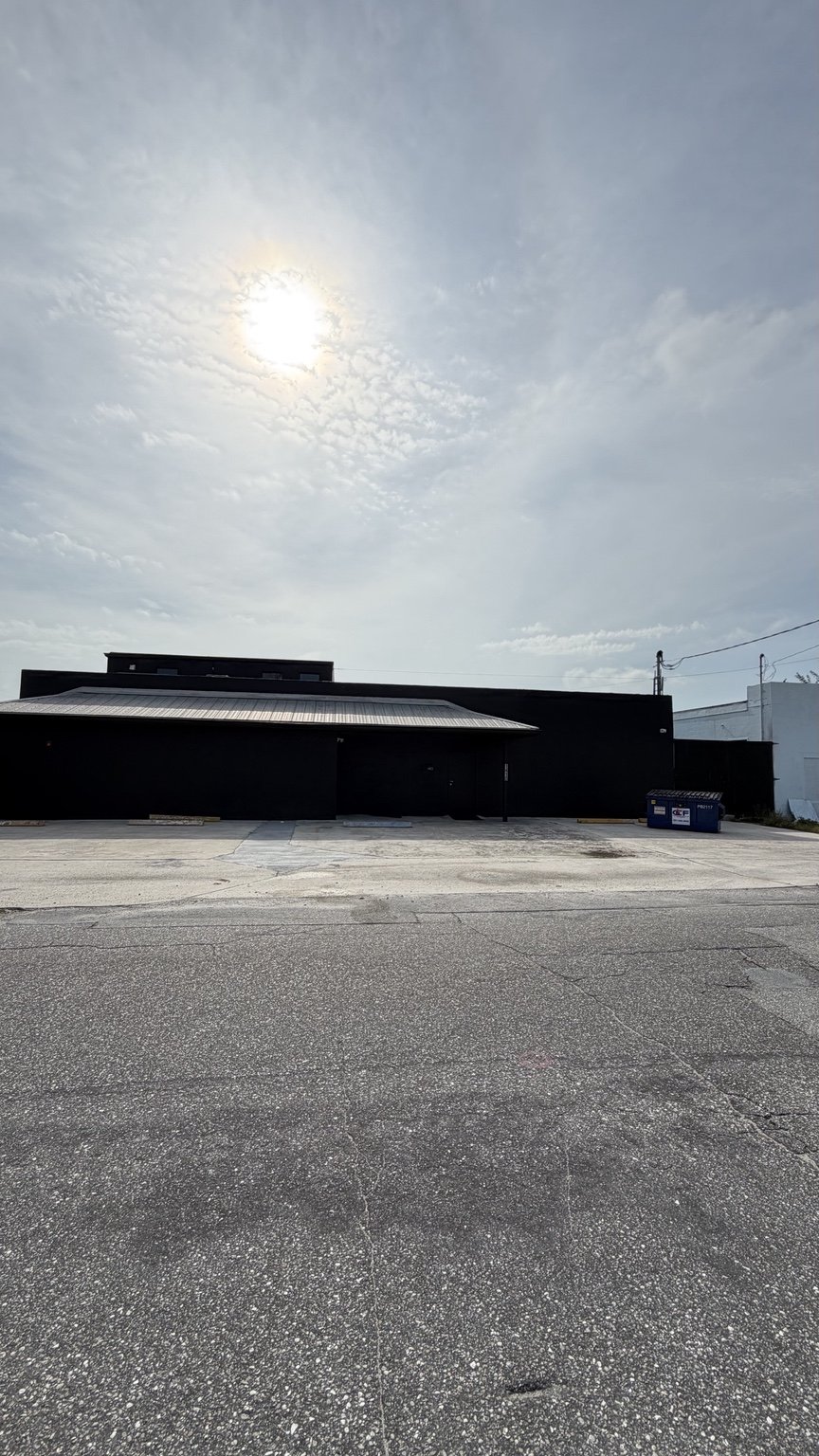 Street-facing black building and covered entrance before the blue and gold mural
