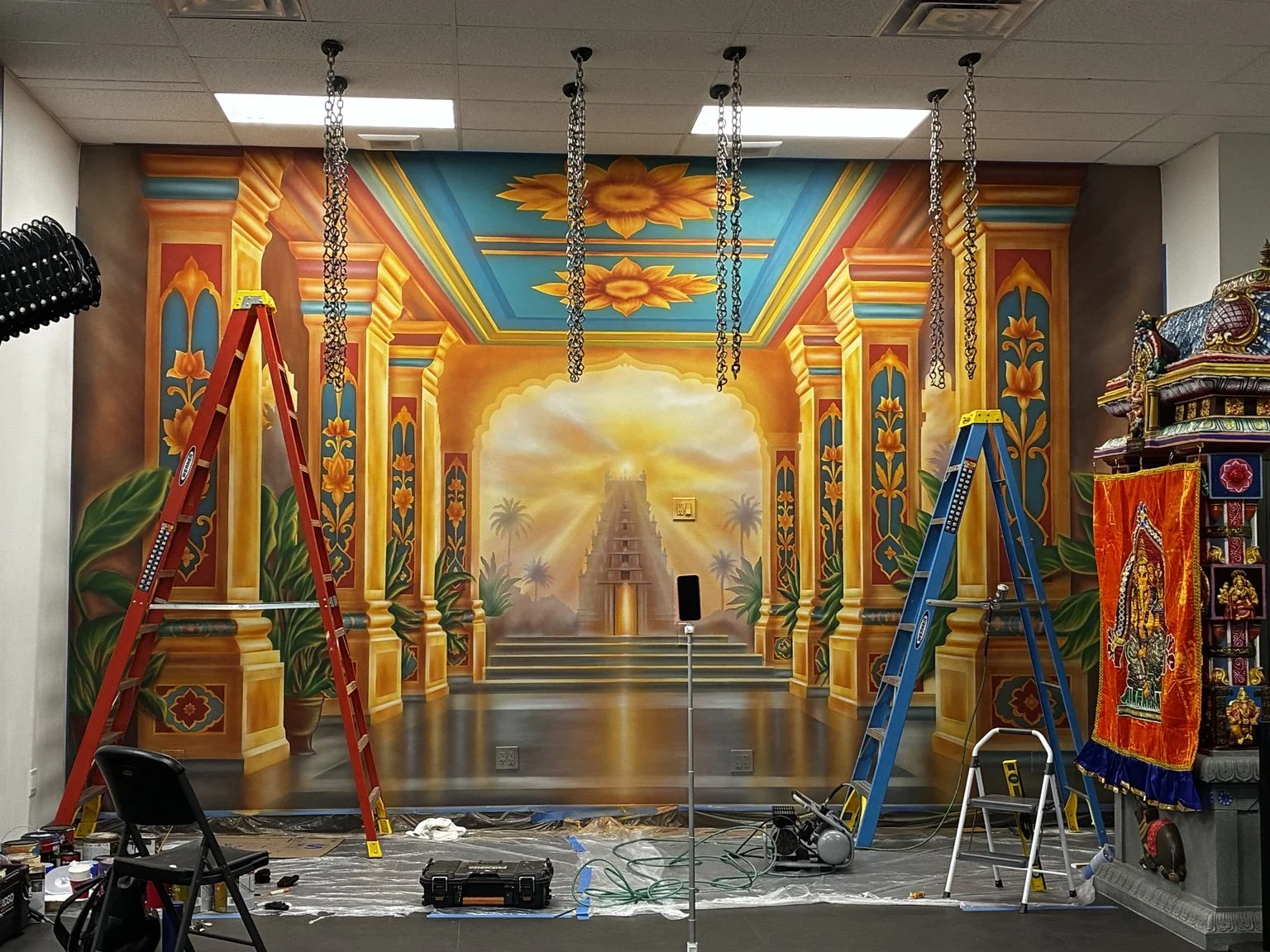 Airbrush and brushwork stage of the Sri Maha Mariamman Temple mural, with ladders and painting equipment visible