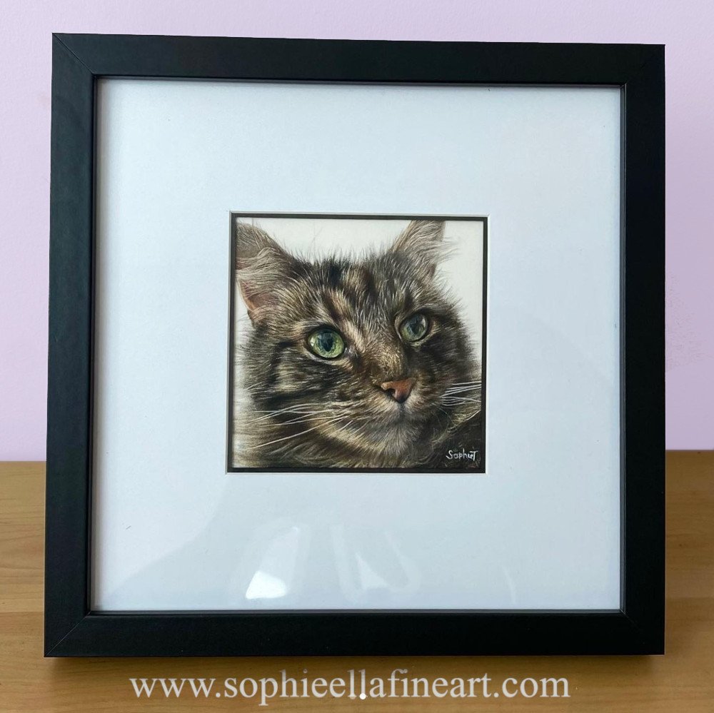 A 4x4 inch mini pet portrait of a cat in a black frame sitting on a wooden shelf with